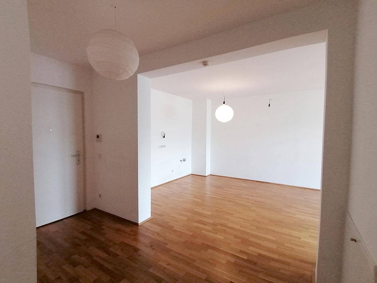 Geräumiges Wohnzimmer mit hellem Parkettboden und weiß gestrichenen Wänden.