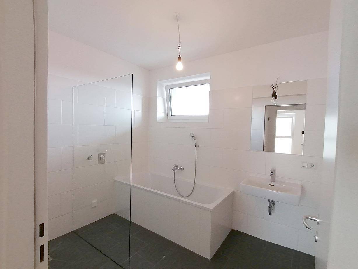 Modernes Badezimmer mit Badewanne, Dusche und Fenster für natürliche Belüftung.