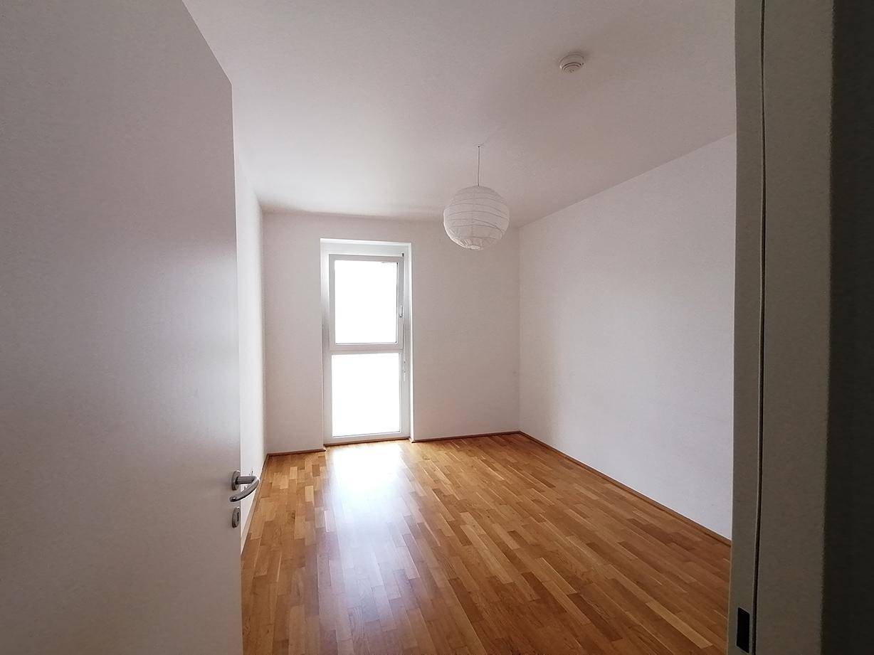Leeres Schlafzimmer mit Parkettboden und großem Fenster für viel Tageslicht.
