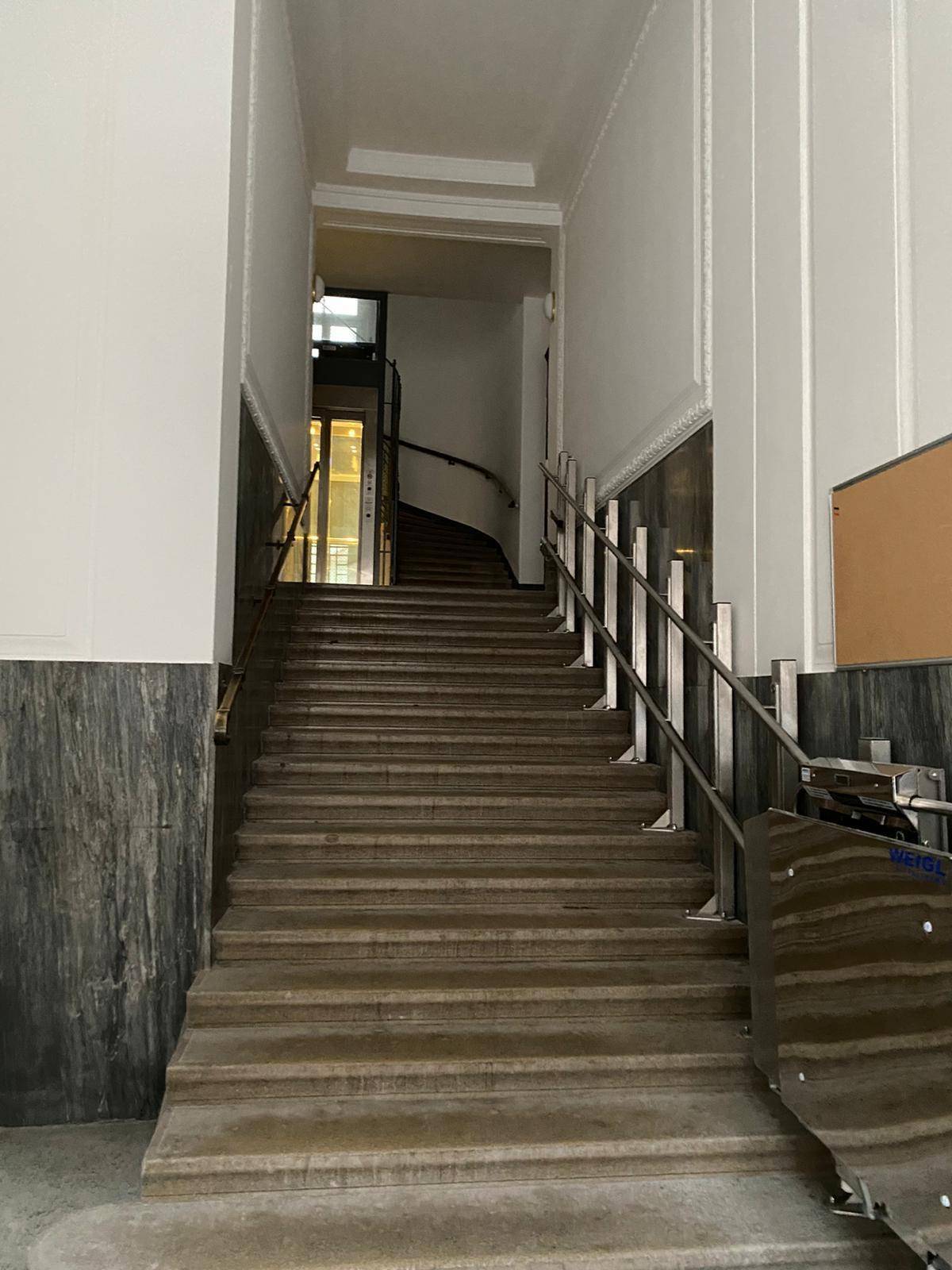 Großzügiges Treppenhaus in einem Altbau mit Steinstufen und eleganten Handläufen.
