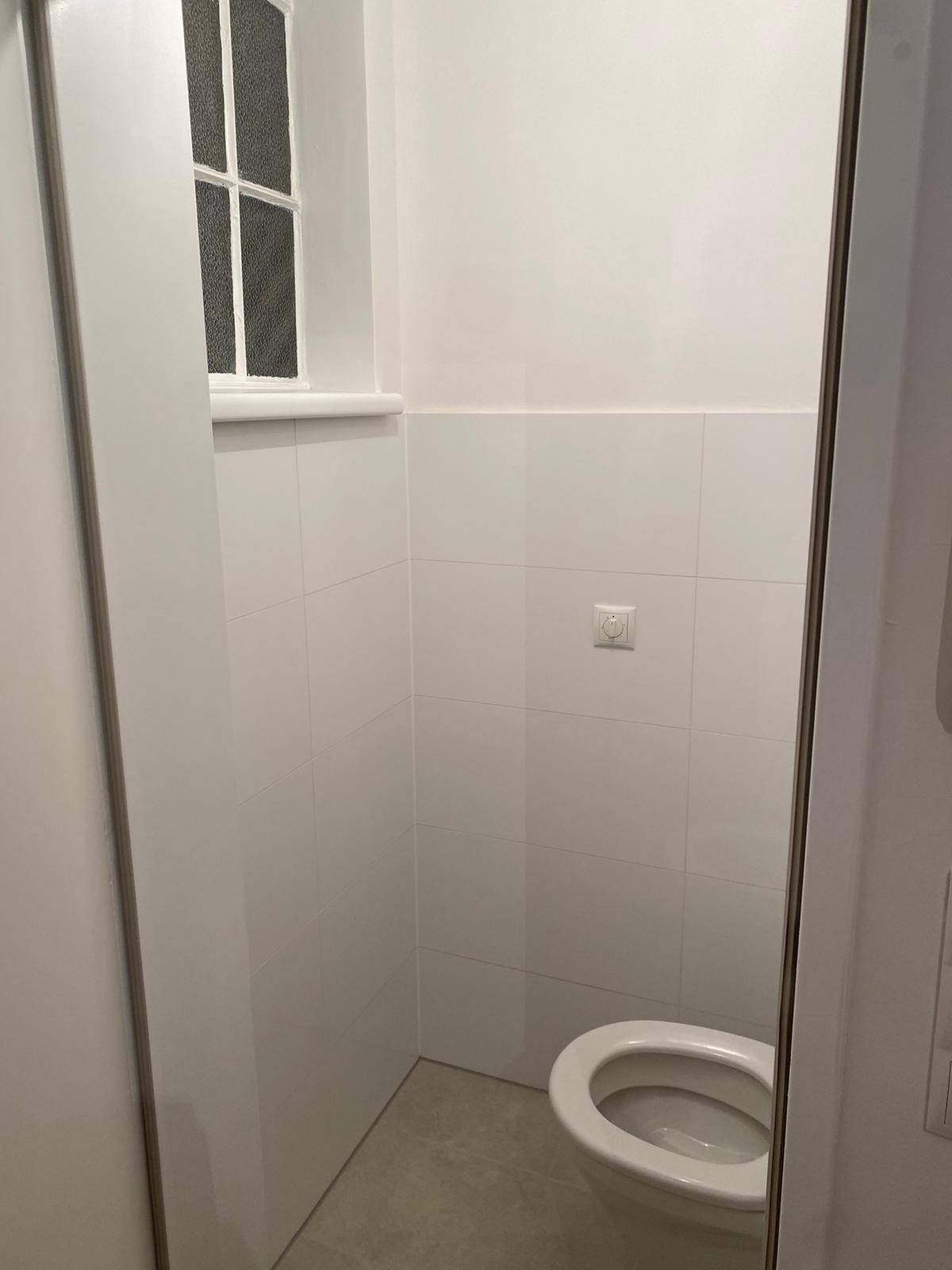 Separate Gästetoilette mit Fenster, weißen Wandfliesen und einem modernen WC.