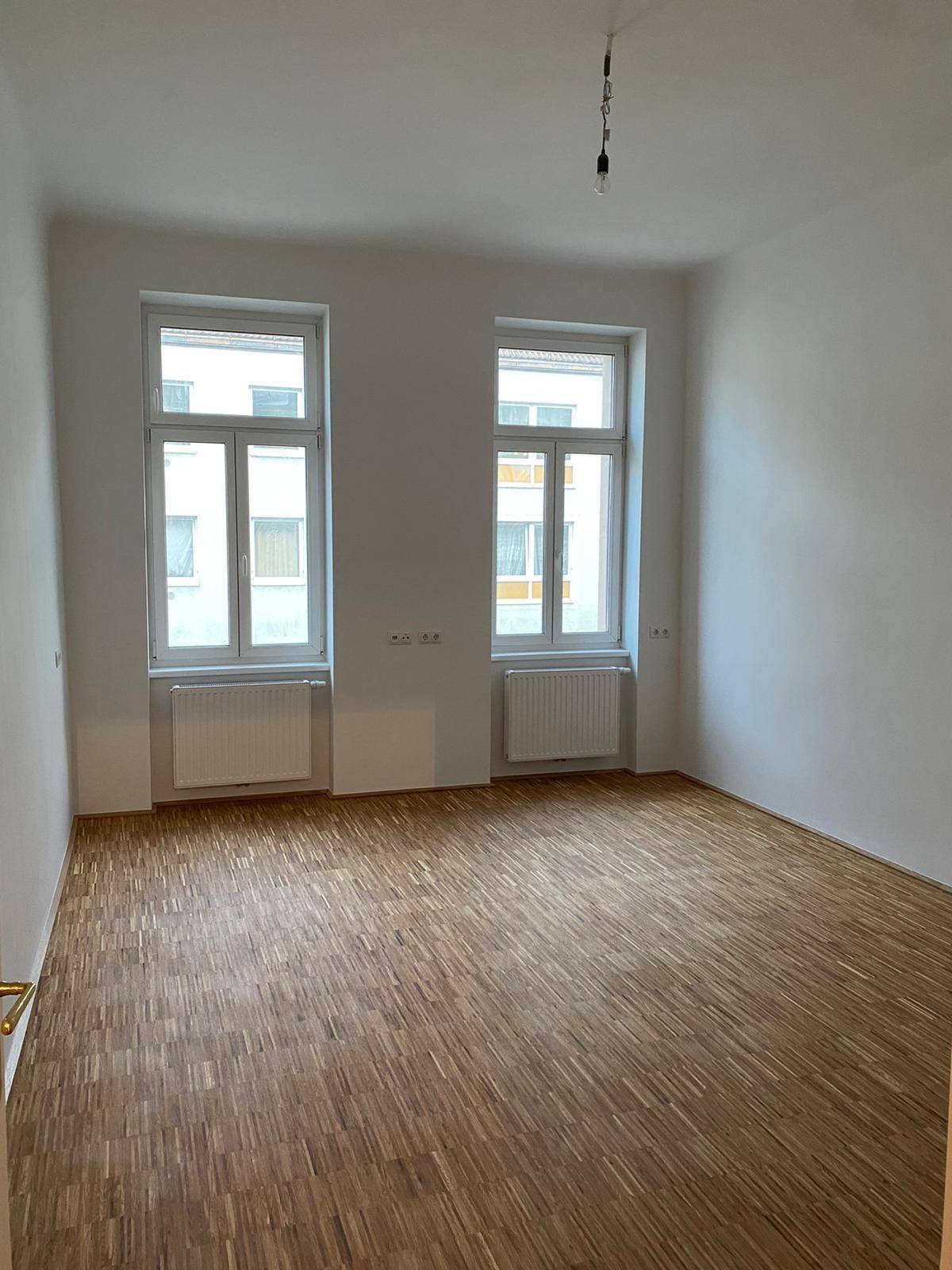 Geräumiges, helles Zimmer mit Parkettboden und Blick auf die umliegenden Gebäude.
