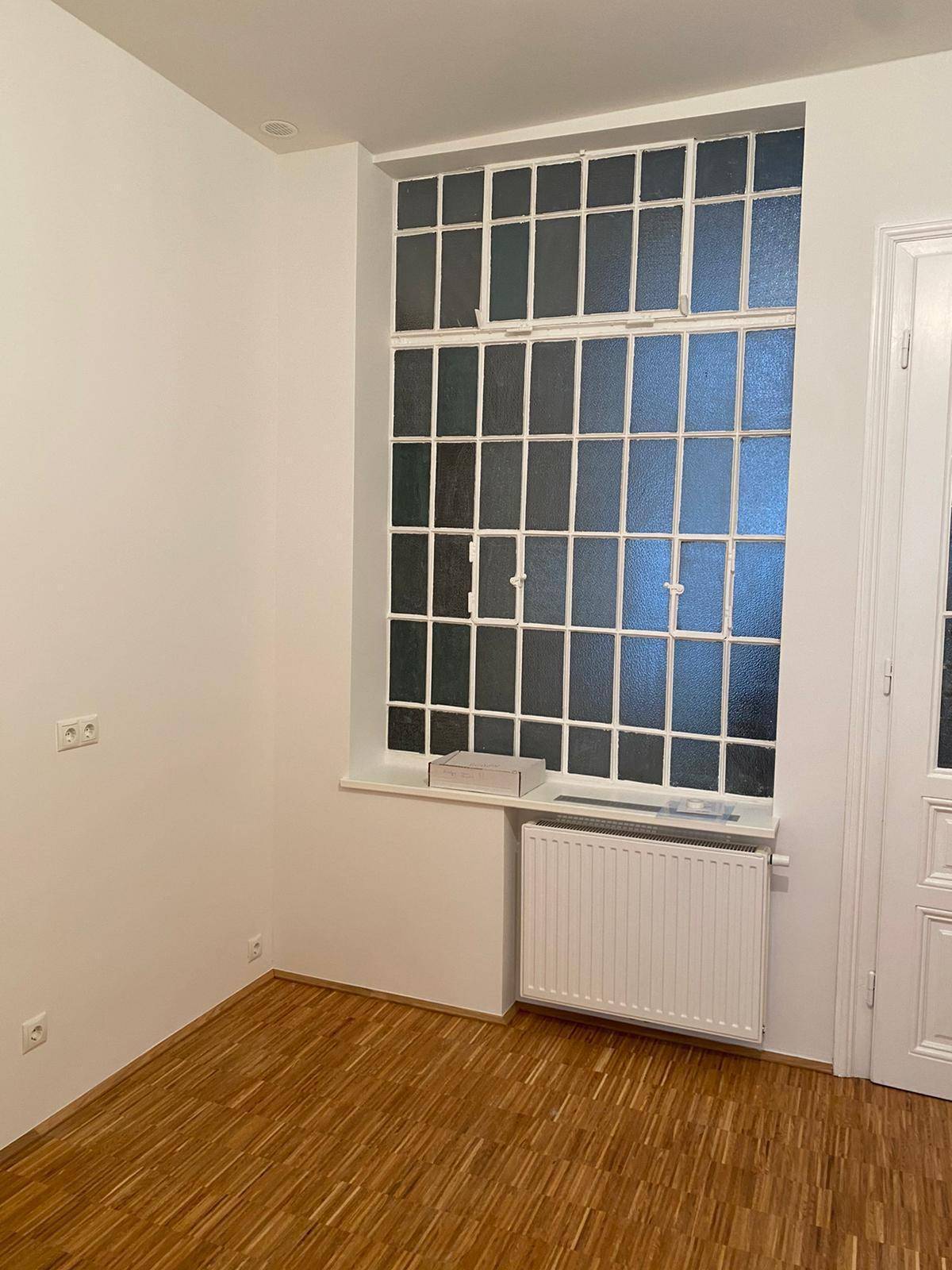 Leerer Raum mit einem großen, mehrteiligen Fenster und einem Heizkörper darunter.