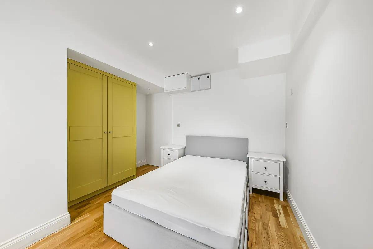 Schlafzimmer mit Holzboden, Doppelbett und einem auffälligen gelben Einbauschrank.