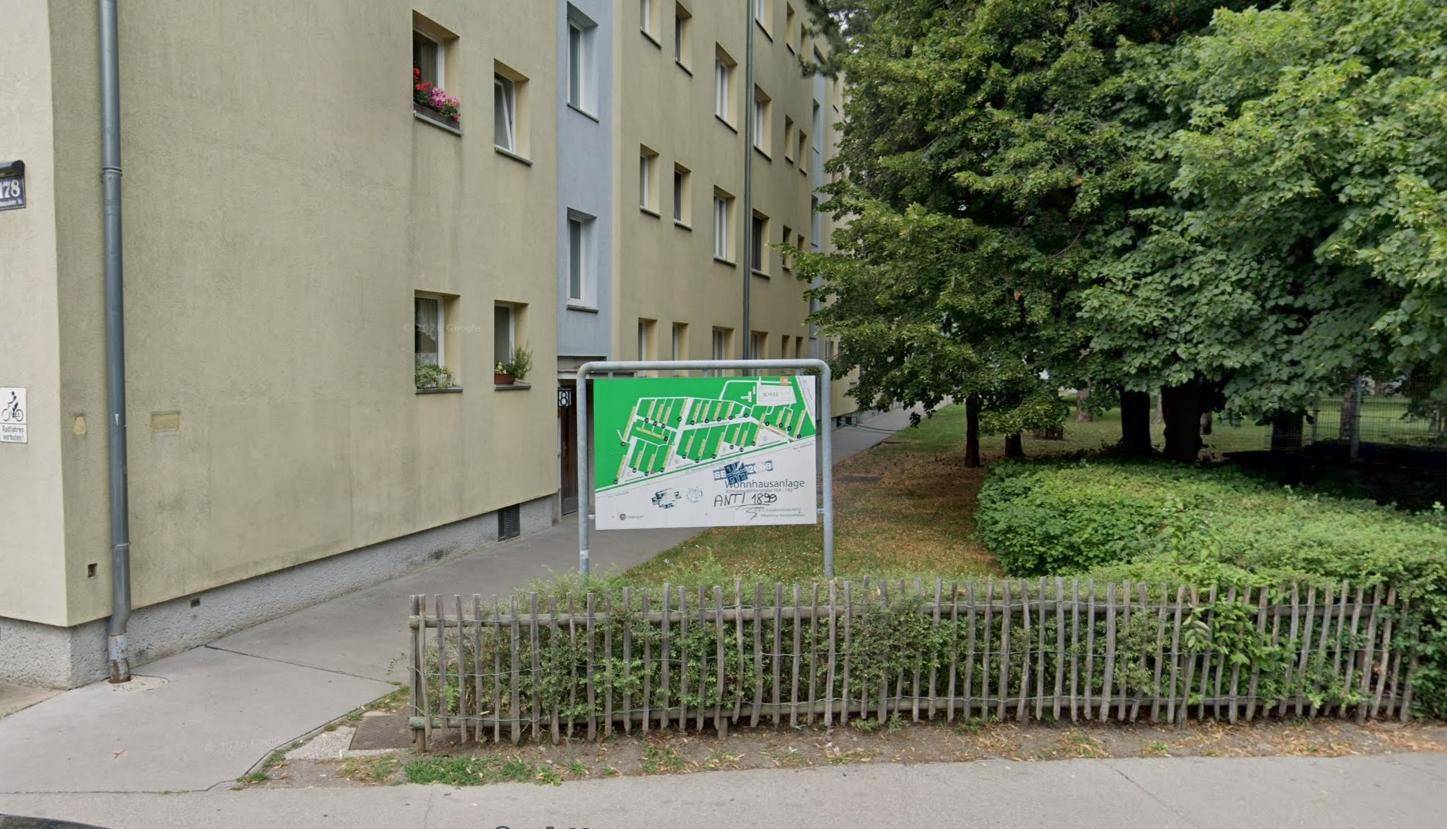Seitenansicht eines Wohngebäudes mit Grünflächen und einem Informationsschild im Vordergrund.