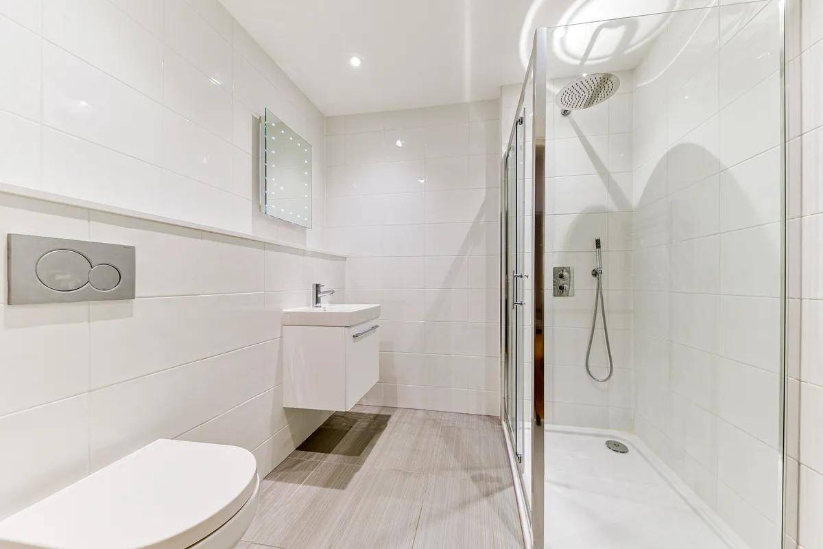 Modernes Badezimmer mit weißen Fliesen, wandhängendem WC und einer geräumigen Duschkabine.
