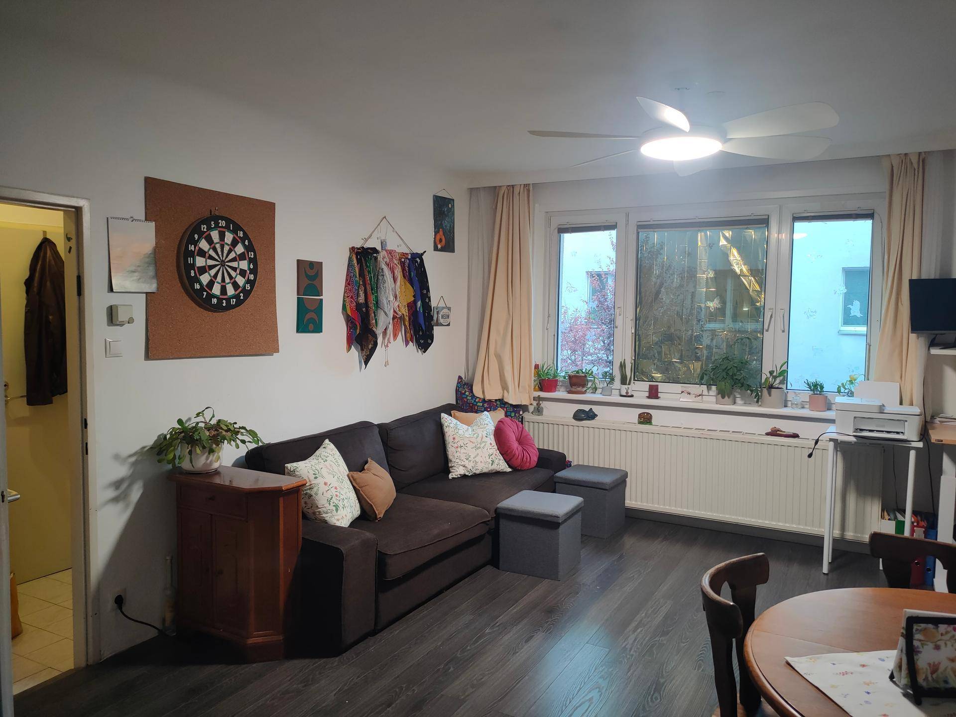 Gemütliches Wohnzimmer mit Sofa, dunklem Laminatboden und Blick ins Grüne durch das Fenster.