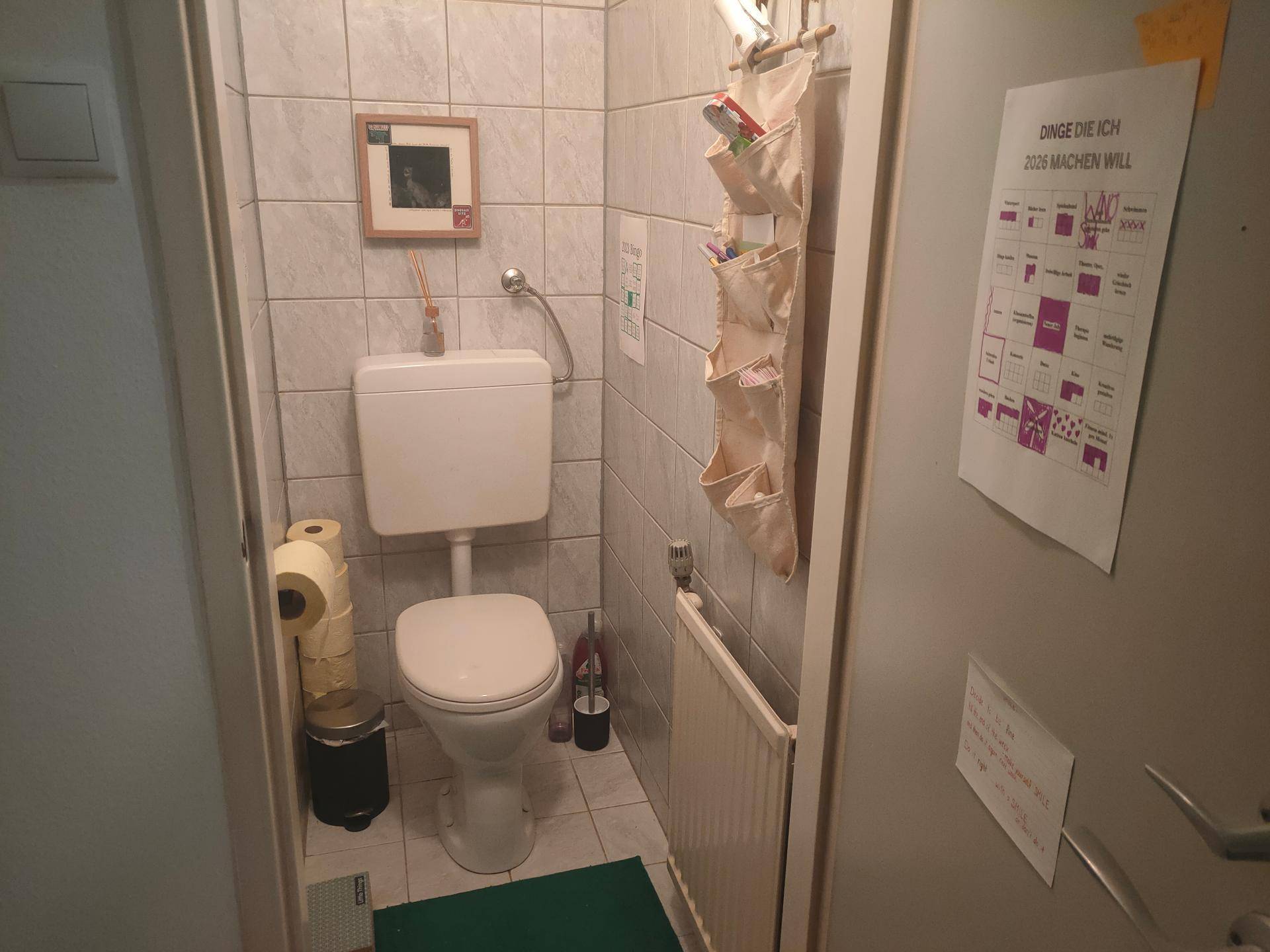 Separates WC mit Toilette, Heizkörper und Fliesen an Wänden und Boden.
