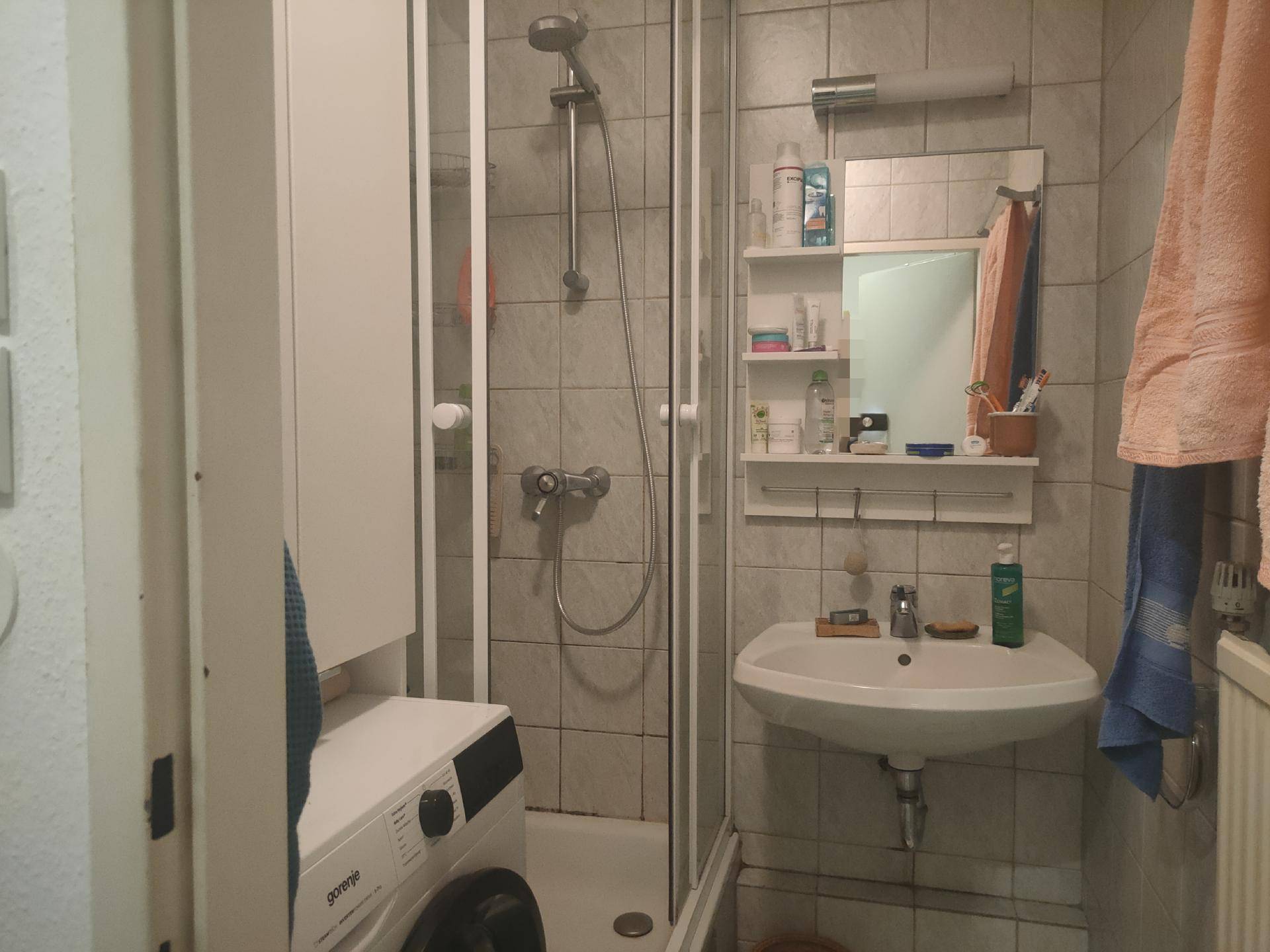 Badezimmer mit Duschkabine, Waschbecken und Fliesen an Wänden und Boden.