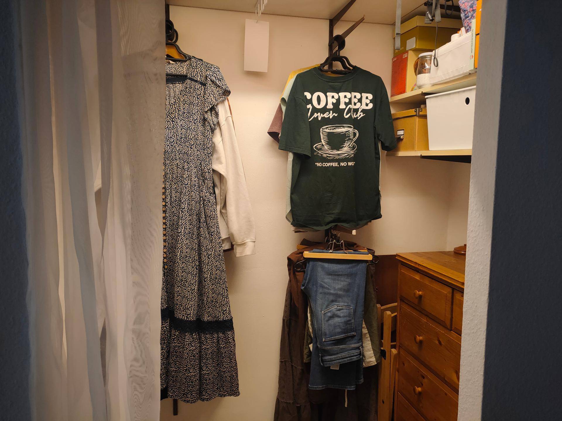 Kleiner begehbarer Kleiderschrank mit Kleidung und einer Holzkommode.