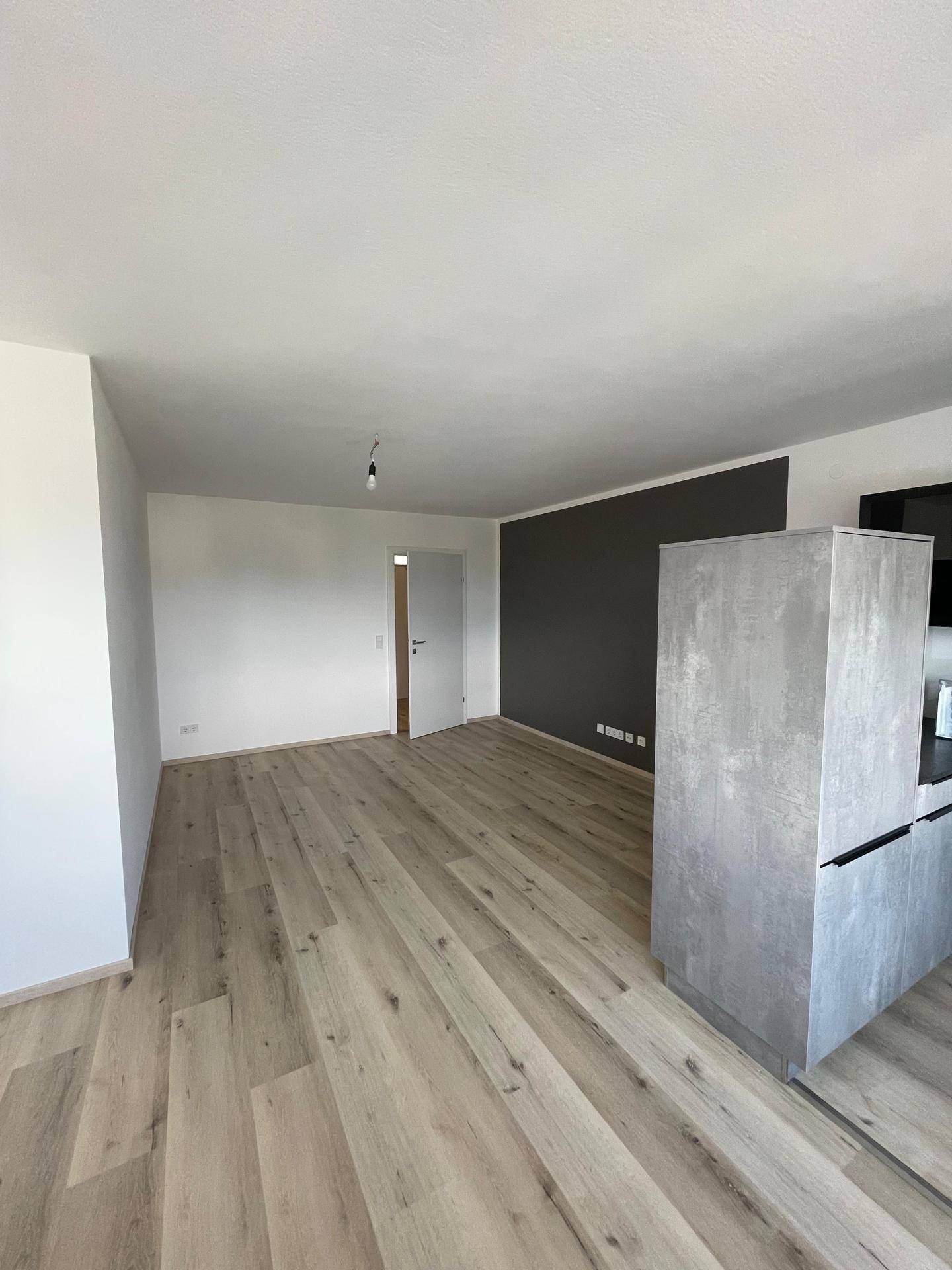 Heller offener Wohnbereich mit modernem Laminatboden, dunkler Akzentwand und Kücheninsel.