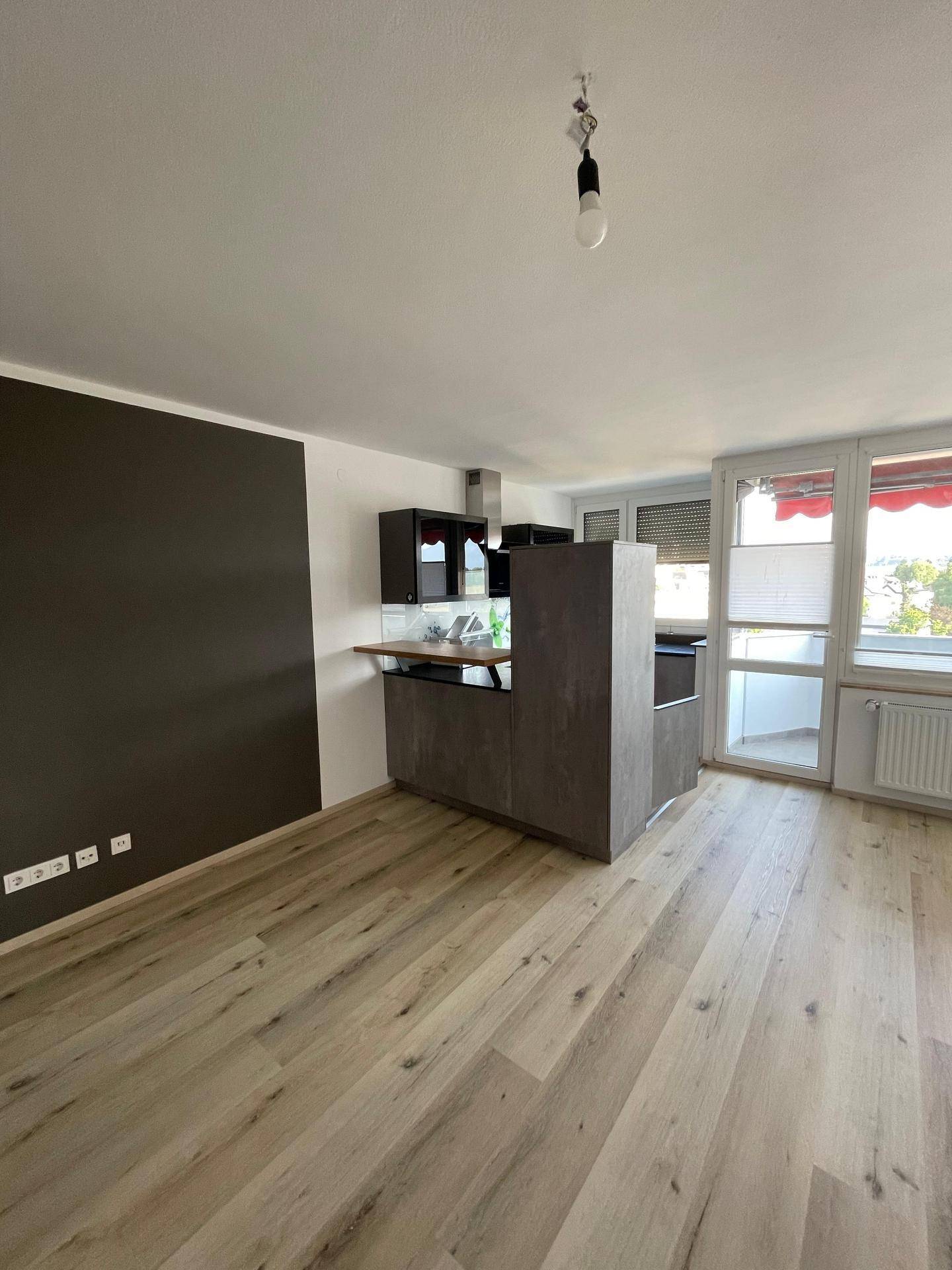 Offener Wohnbereich mit Küchenzeile, Laminatboden und direktem Zugang zum Balkon.