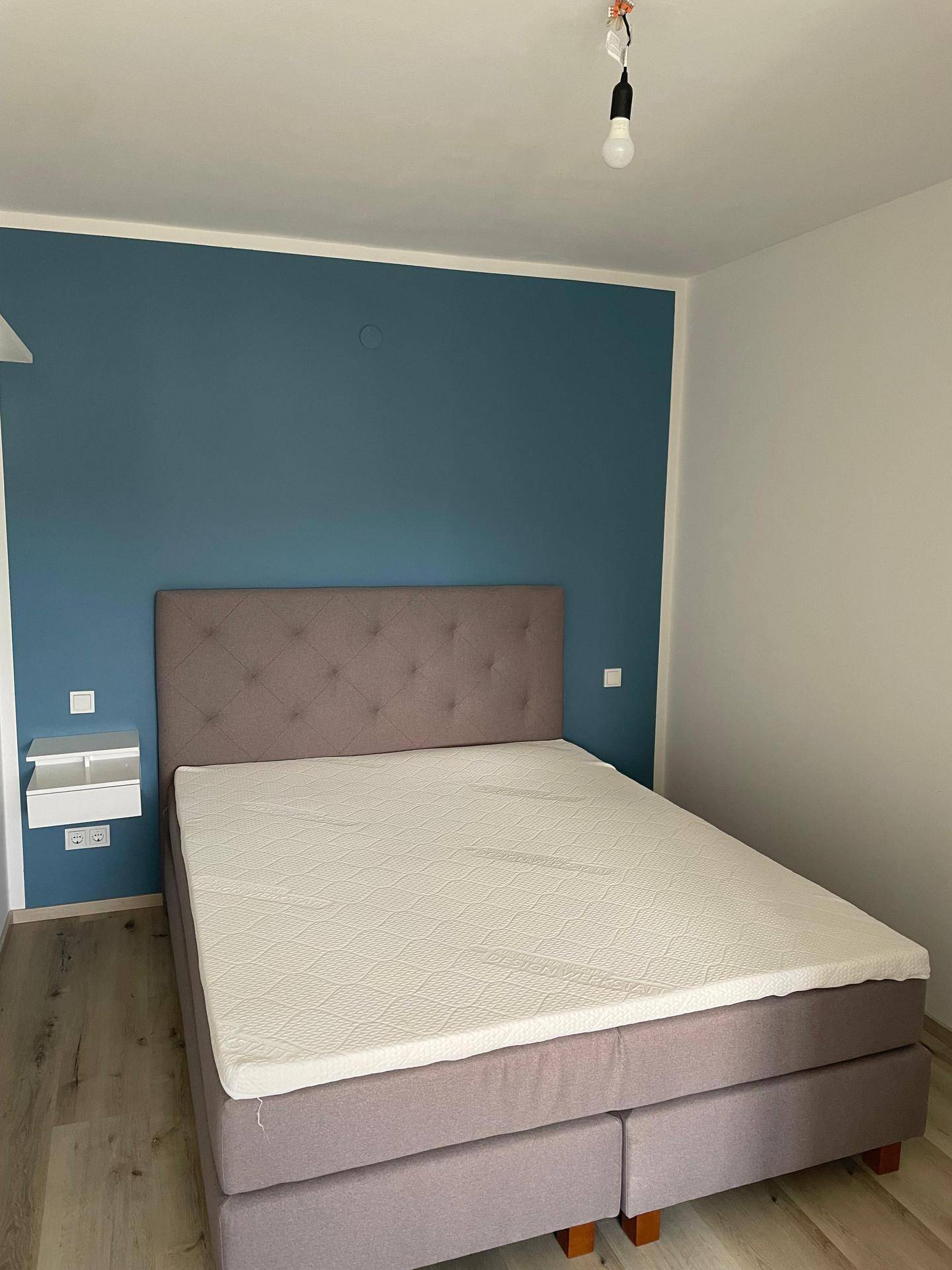 Gemütliches Schlafzimmer mit blauer Akzentwand, Doppelbett und hellem Laminatboden.