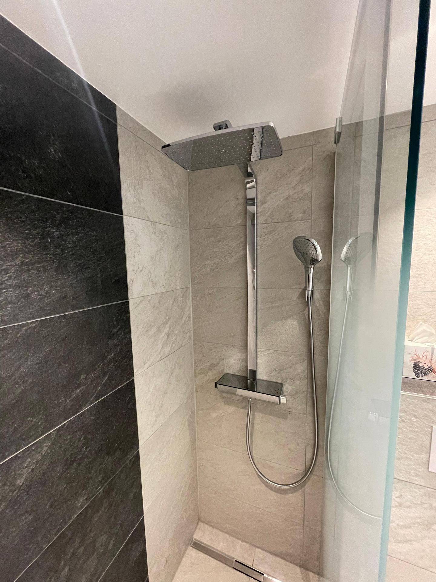 Modernes Badezimmer mit begehbarer Dusche, Regenduschkopf und grauen Fliesen an den Wänden.