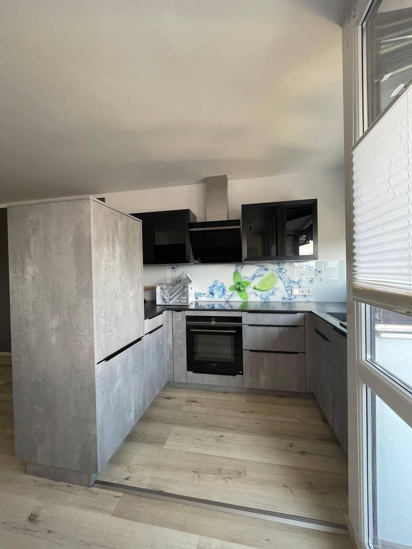 Moderne Einbauküche mit grauen Fronten, schwarzen Geräten, Backofen und Dunstabzugshaube.
