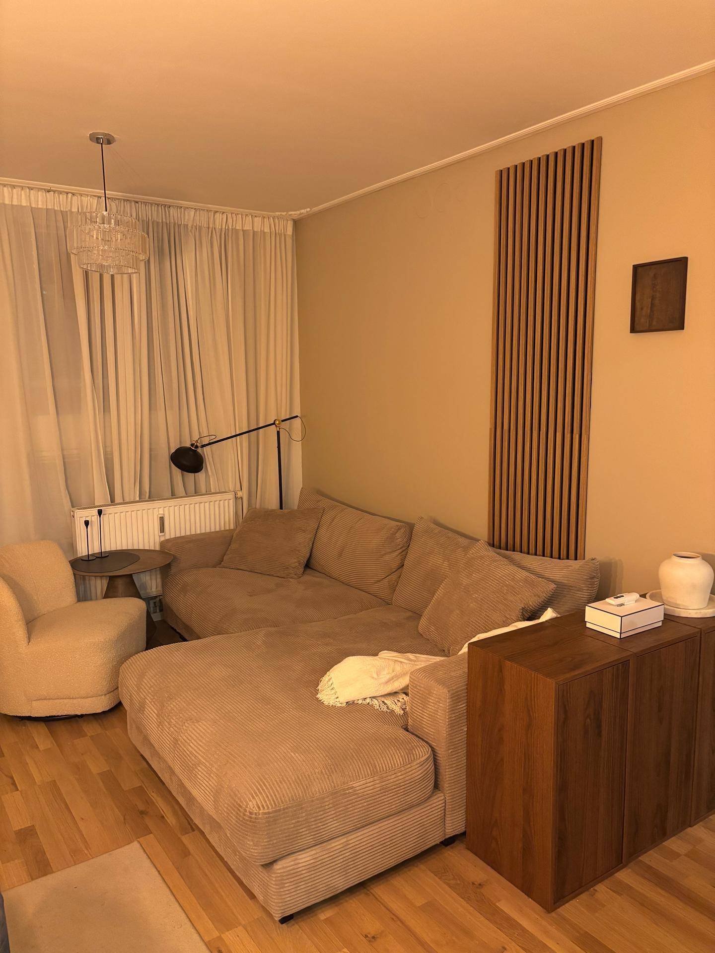 Geräumiges Wohnzimmer mit beigem Ecksofa, Holzmöbeln und dekorativer Wandverkleidung.