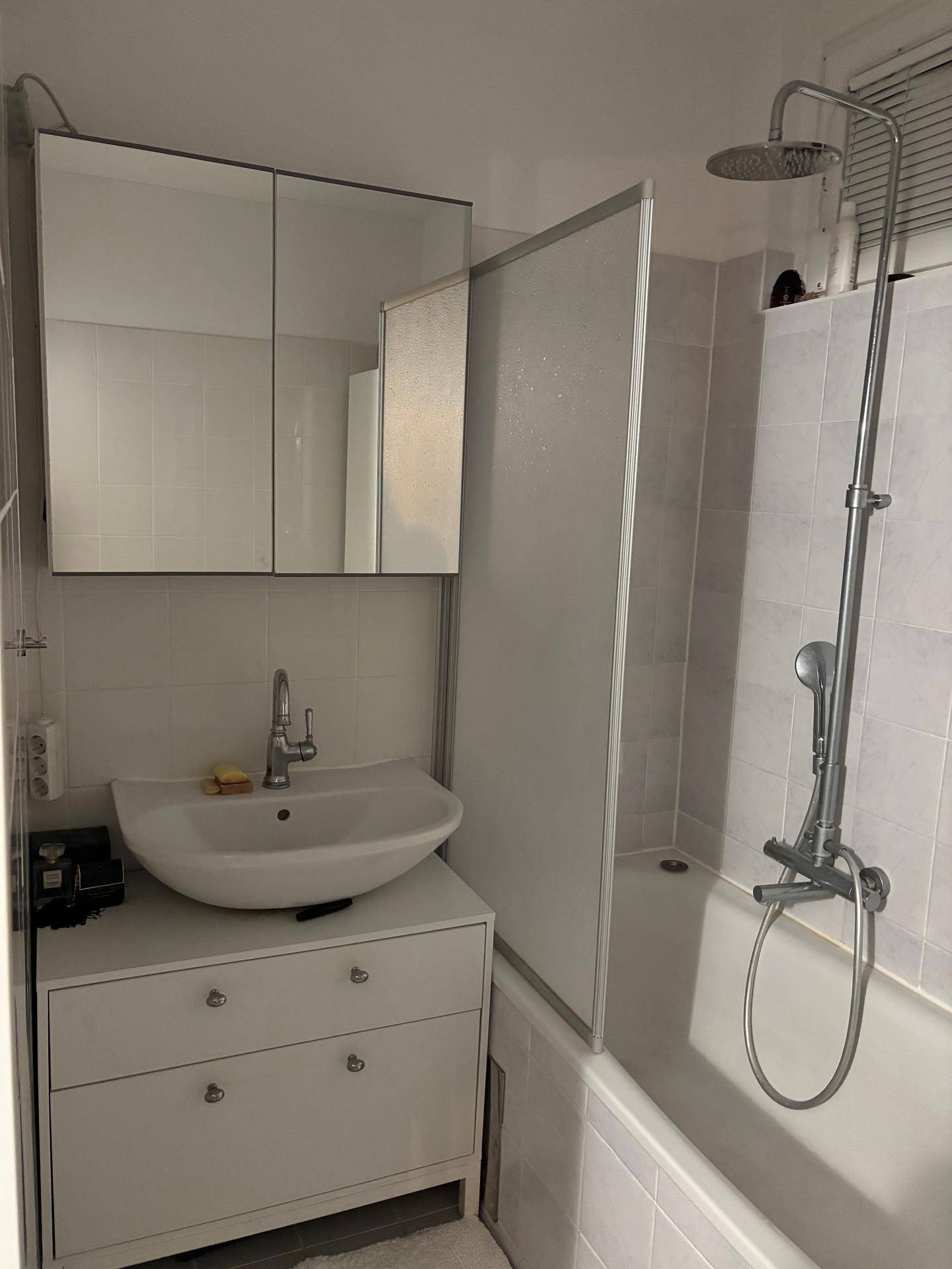 Badezimmer mit Waschbecken, Spiegelschrank und Badewanne mit Duschfunktion.