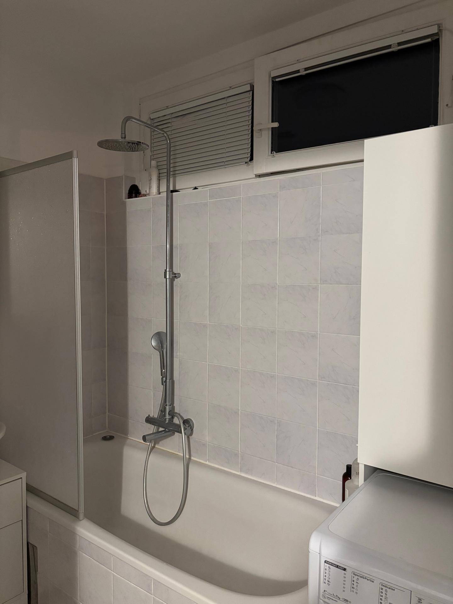 Helles Badezimmer mit Badewanne, Duscharmatur und Fenster für Tageslicht.