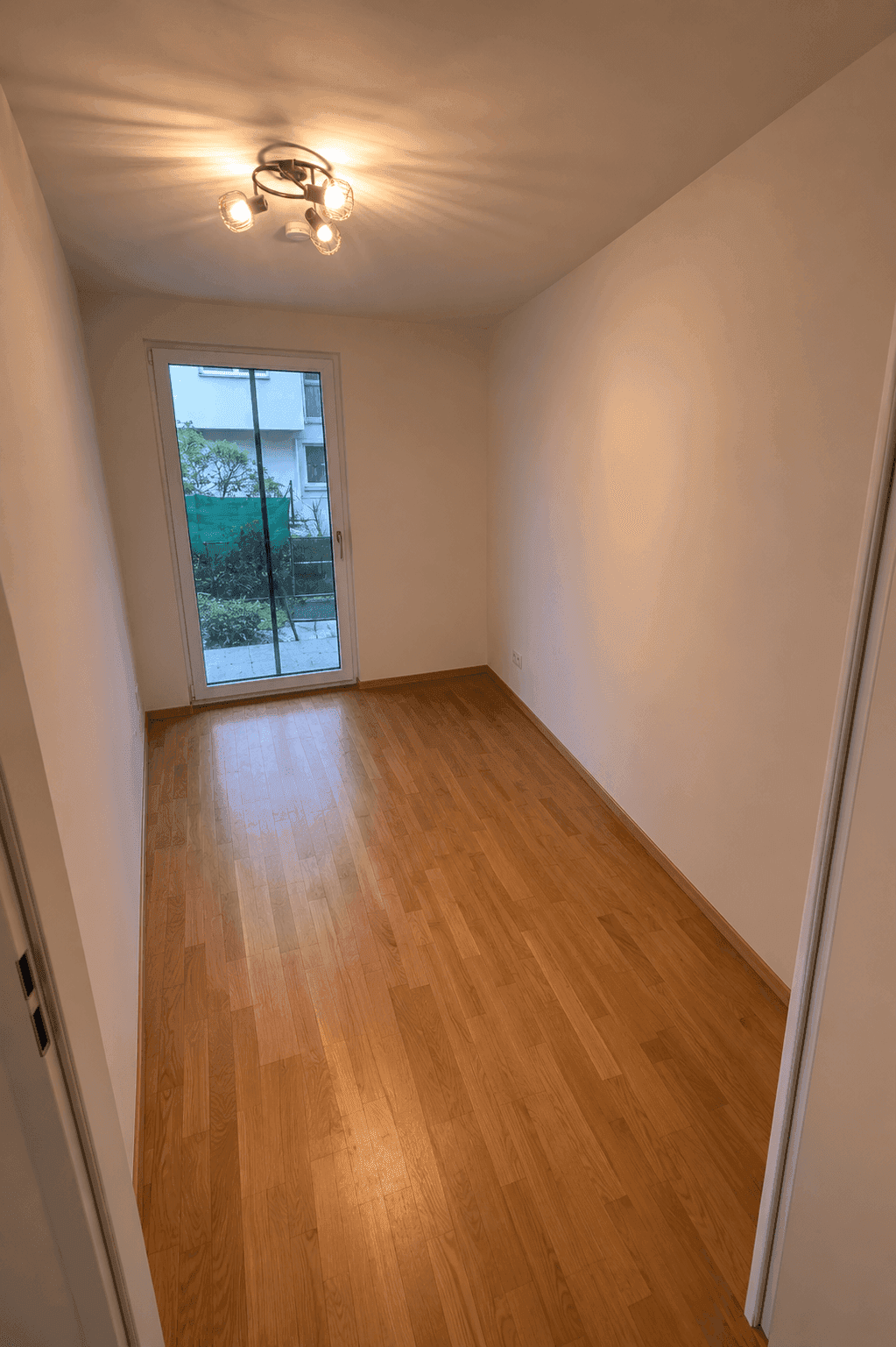 Helles Zimmer mit Holzboden und Zugang zu einem kleinen Außenbereich.