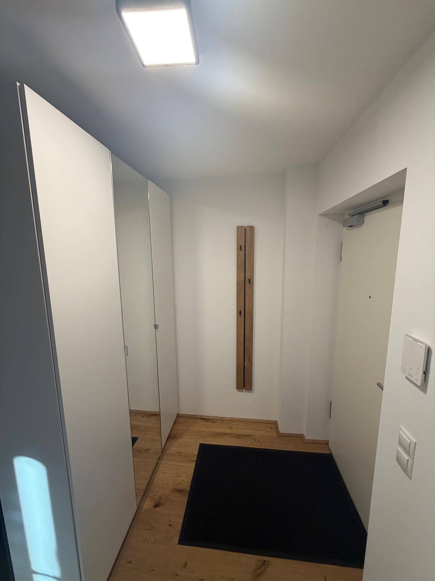 Eingangsbereich mit weißem Einbauschrank, Spiegeltür und Holzboden.