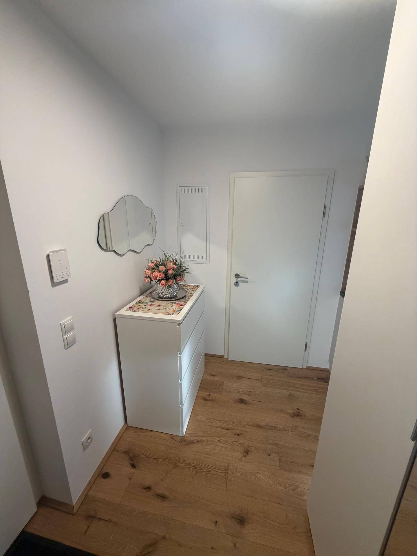 Heller Flur mit Holzboden, weißer Kommode und einem dekorativen Spiegel.