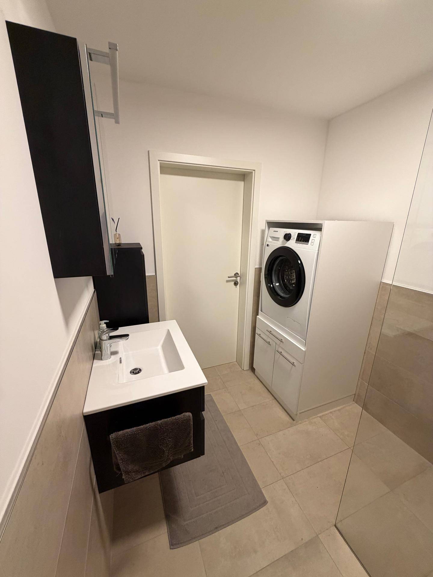 Modernes Badezimmer mit Waschbecken, Waschmaschine und ebenerdiger Dusche.