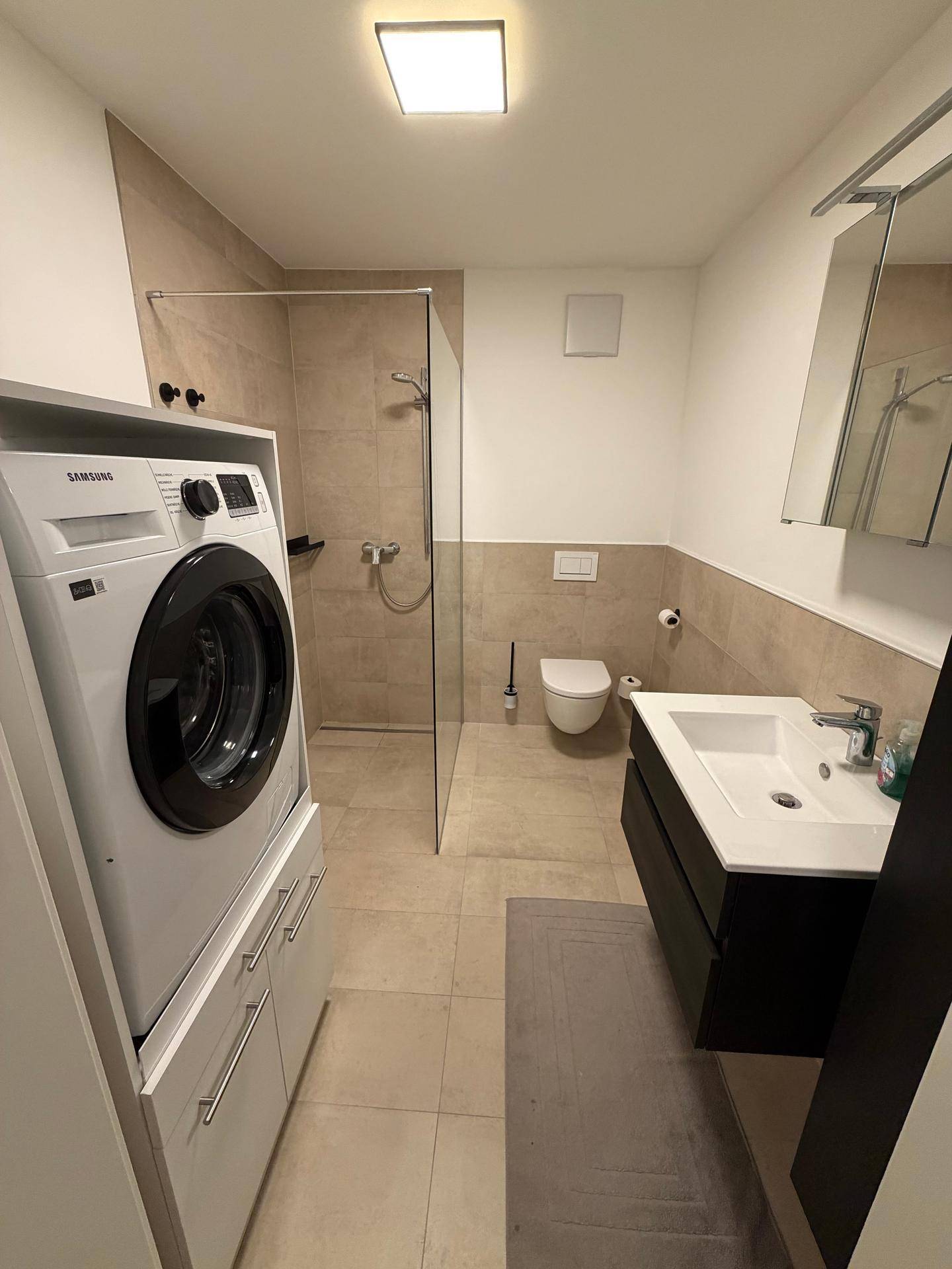 Modernes Badezimmer mit ebenerdiger Dusche, Waschbecken und Waschmaschine.