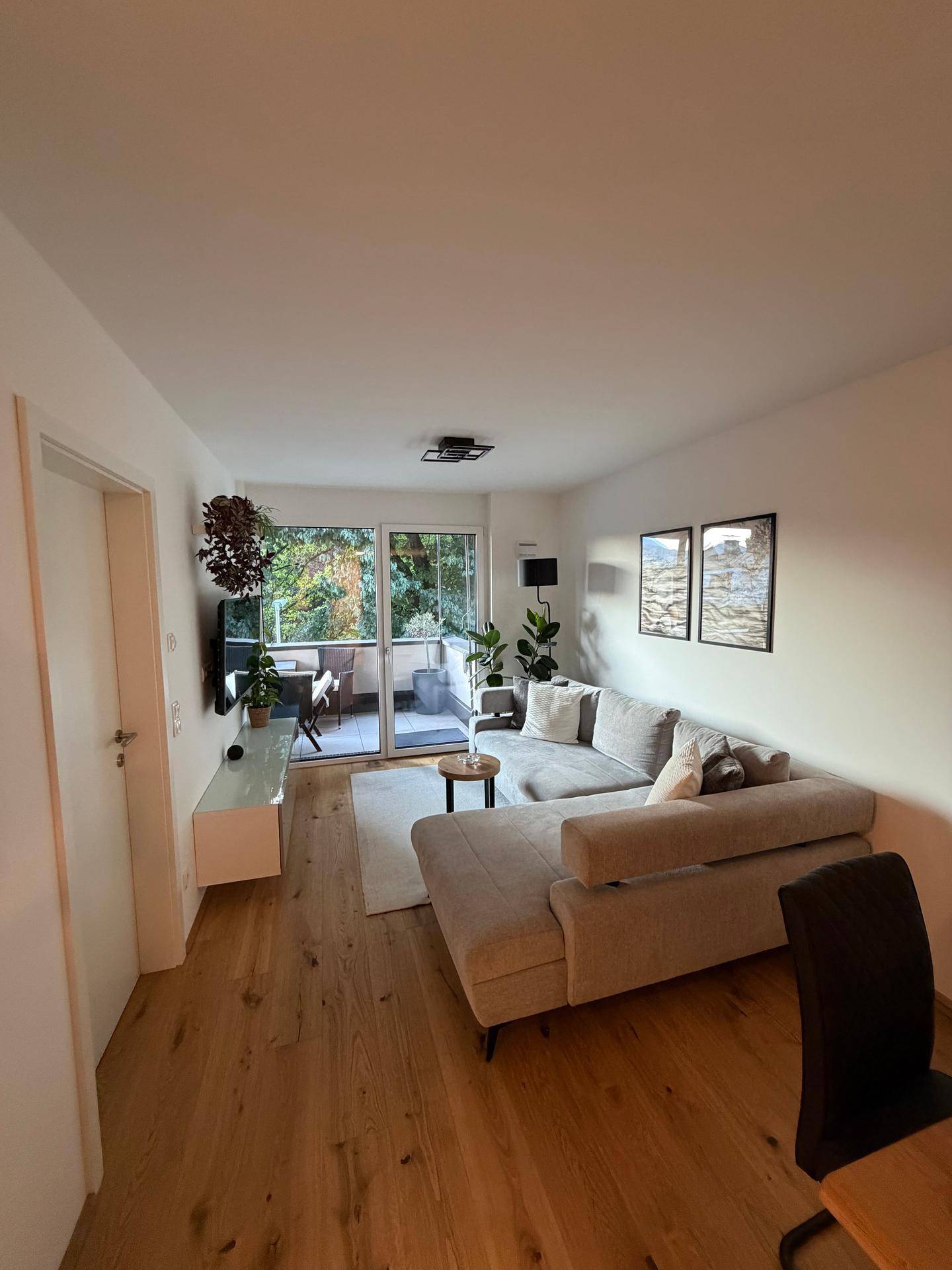 Geräumiges Wohnzimmer mit modernem Ecksofa, Holzboden und Blick ins Grüne vom Balkon.