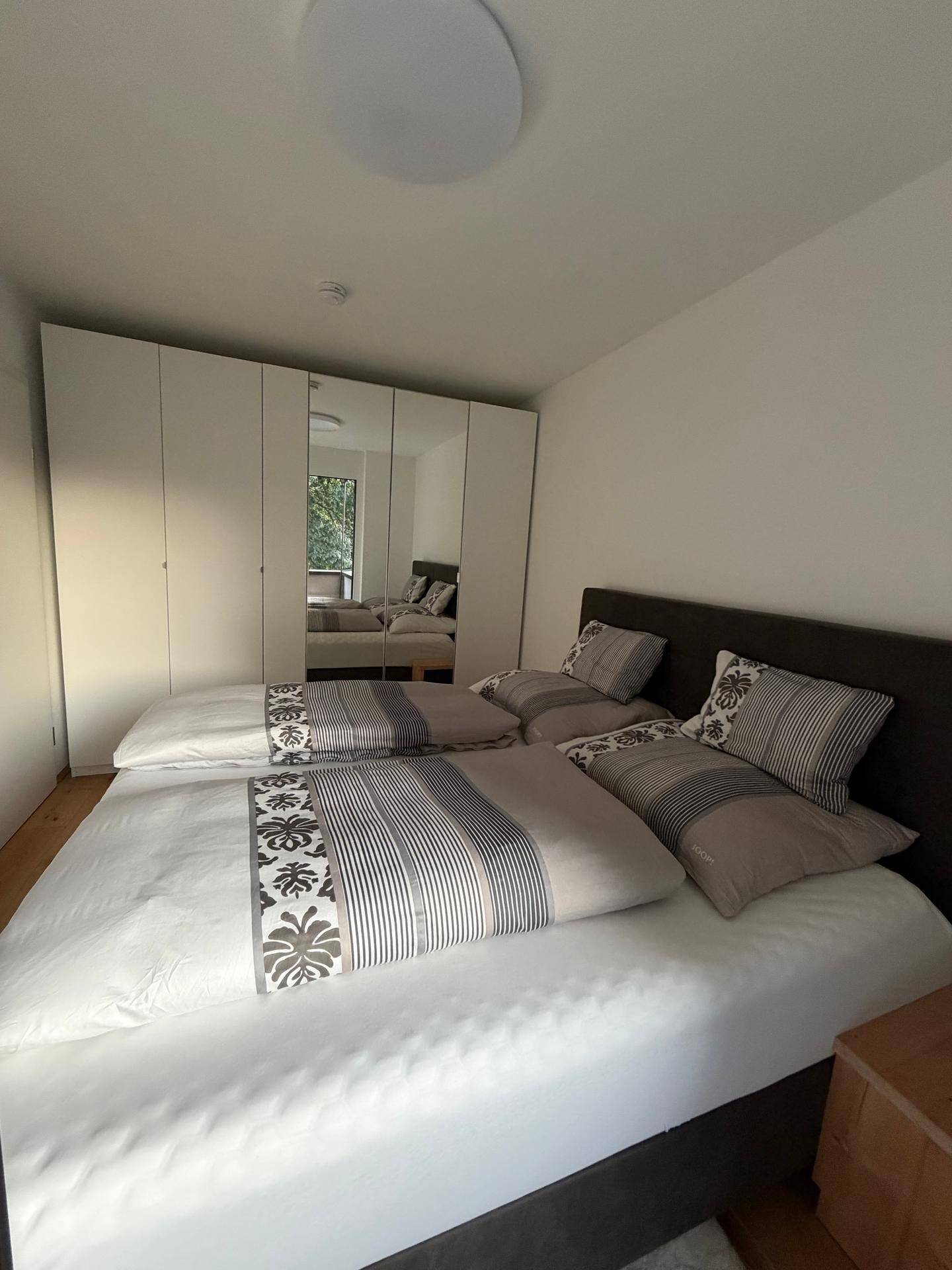 Schlafzimmer mit großem Kleiderschrank, Spiegeltüren und Holzboden.