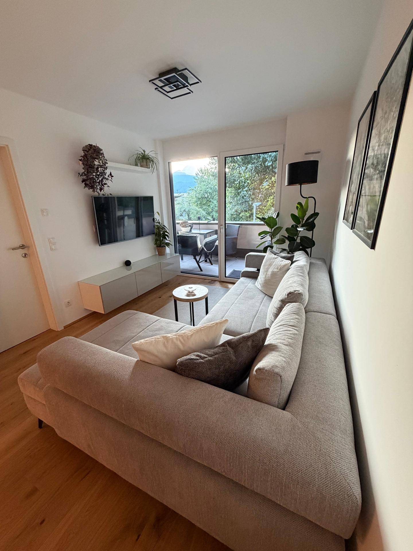 Lichtdurchflutetes Wohnzimmer mit großem Ecksofa, Holzboden und Bergblick vom Balkon.