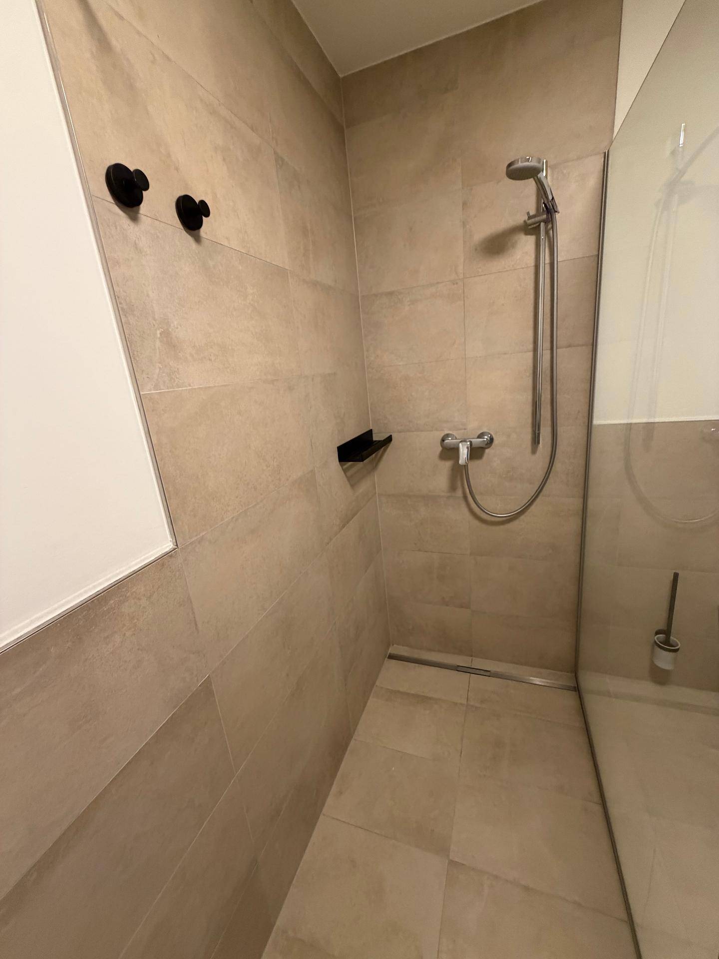 Ebenerdige Dusche mit modernen beigen Fliesen und Duscharmatur.
