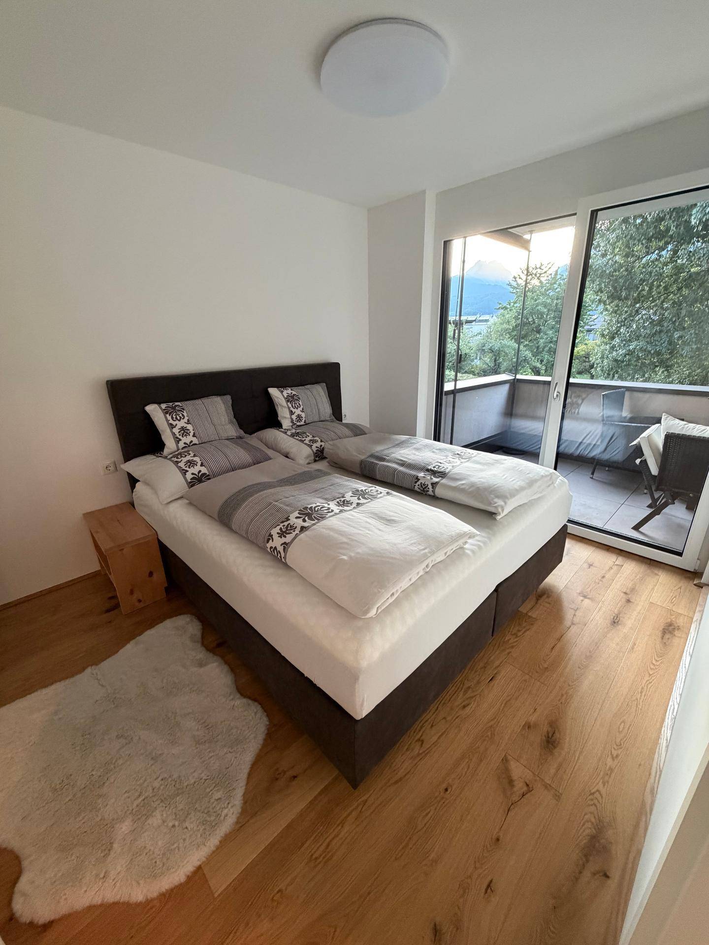 Helles Schlafzimmer mit Doppelbett, Holzboden und direktem Zugang zum Balkon mit Bergblick.