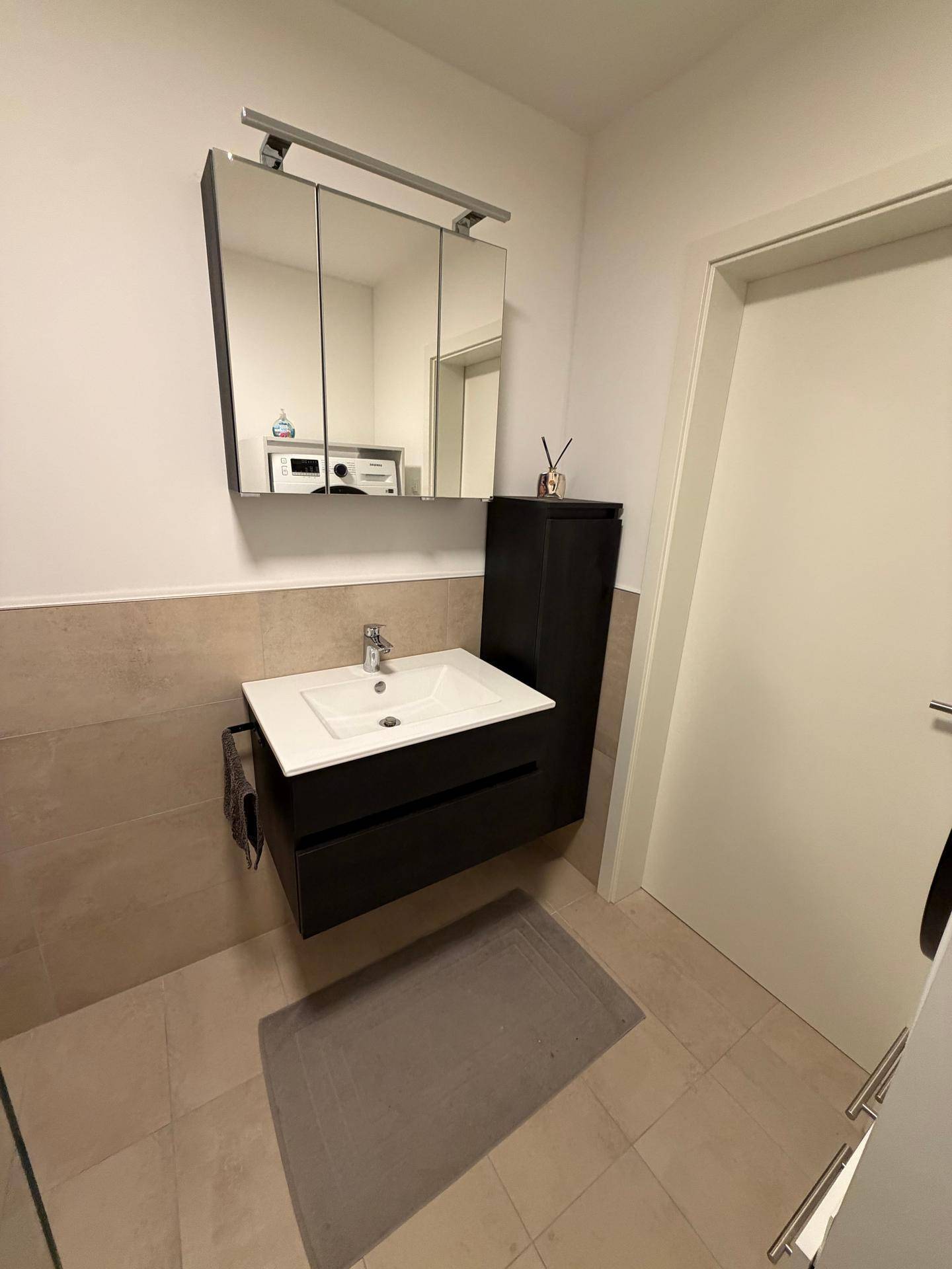 Modernes Badezimmer mit Waschbecken, Spiegelschrank und hellen Fliesen.
