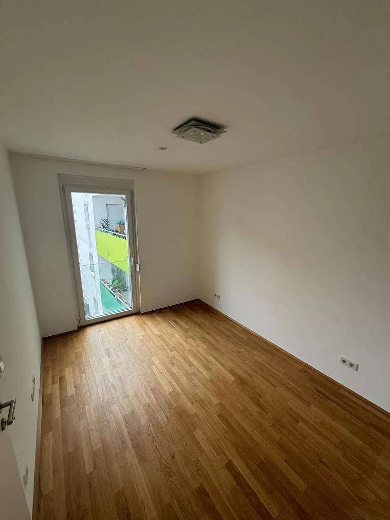 Helles Zimmer mit Parkettboden und direktem Zugang zu einem kleinen Balkon.