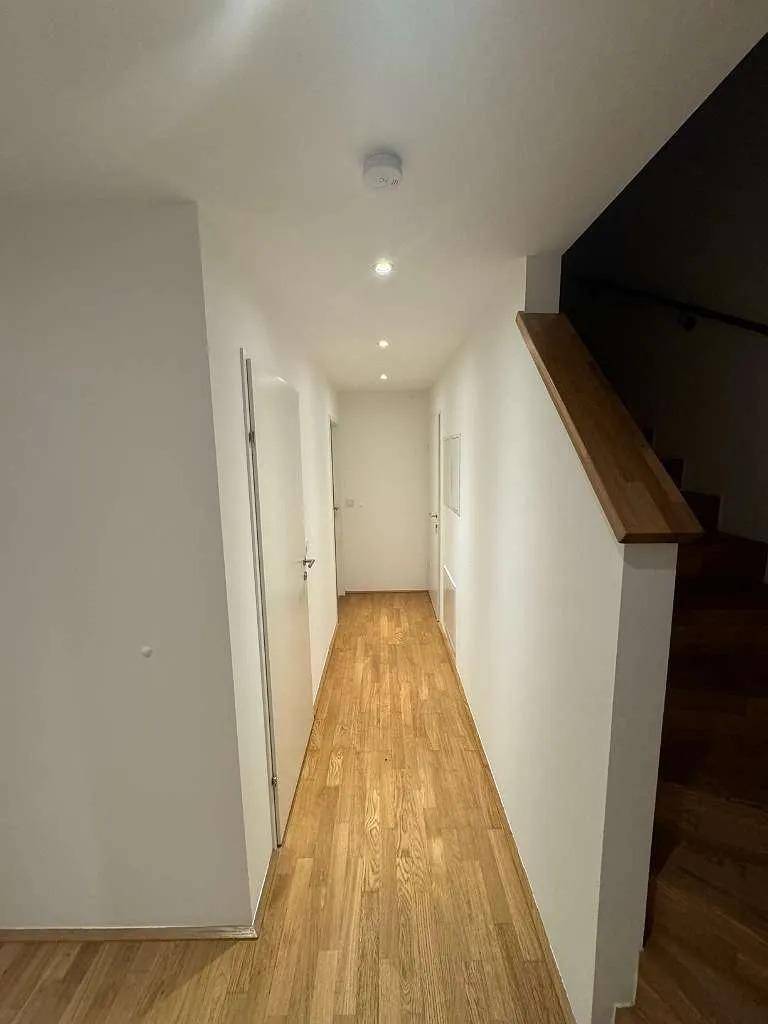 Heller Flur mit Holzparkett und integrierten Deckenleuchten, der zu weiteren Räumen führt.