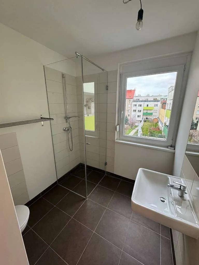 Modernes Badezimmer mit ebenerdiger Dusche, Waschbecken, Toilette und Fenster für Tageslicht.
