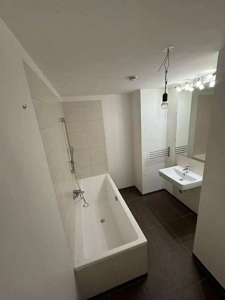 Modernes Badezimmer mit Badewanne, Waschbecken und großem Spiegel, hell gefliest.