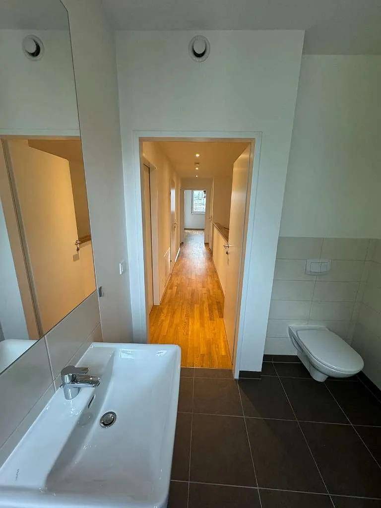 Badezimmer mit Waschbecken, wandhängender Toilette und Blick in den angrenzenden Flur.