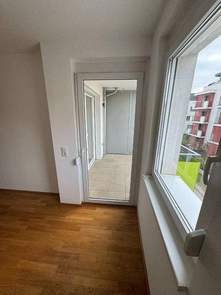 Heller Raum mit Zugang zu einem gefliesten Balkon und Blick auf die Umgebung.