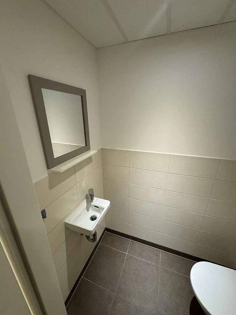 Kleines Gäste-WC mit modernem Waschbecken, Spiegel und hellen Fliesen an Wänden und Boden.