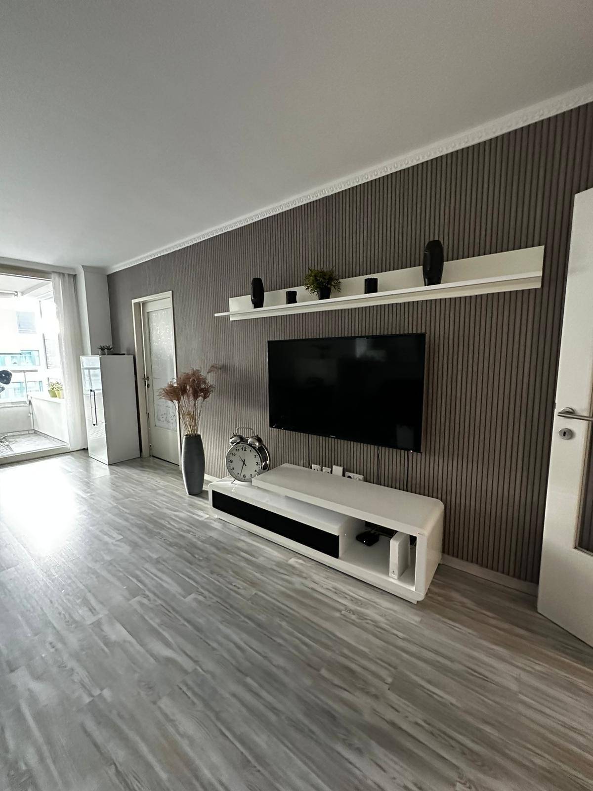 Moderner Wohnbereich mit stilvoller TV-Wand, elegantem Sideboard und Zugang zum Balkon.