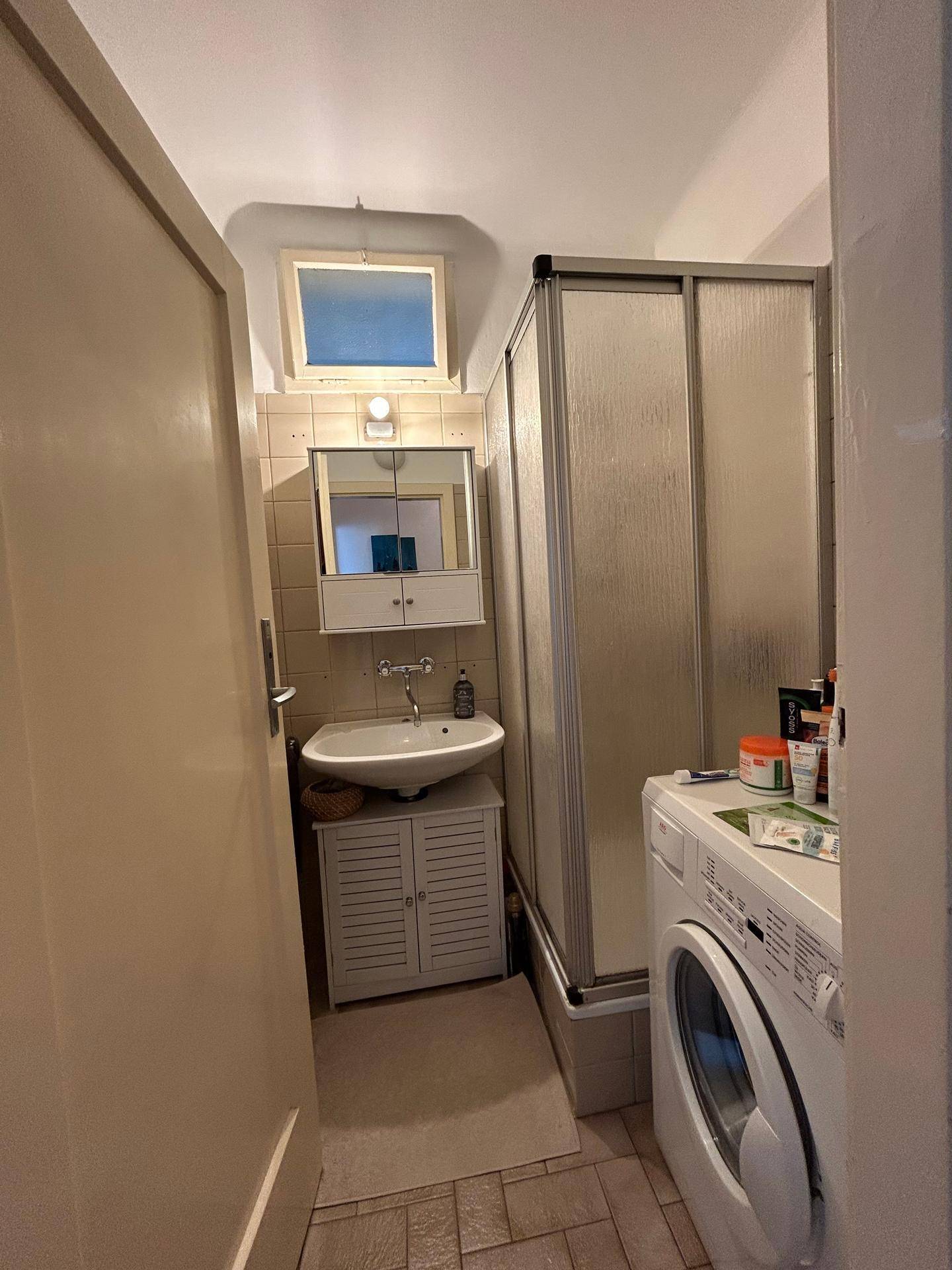 Kleines Badezimmer mit Dusche, Waschbecken und Waschmaschine, praktisch eingerichtet.