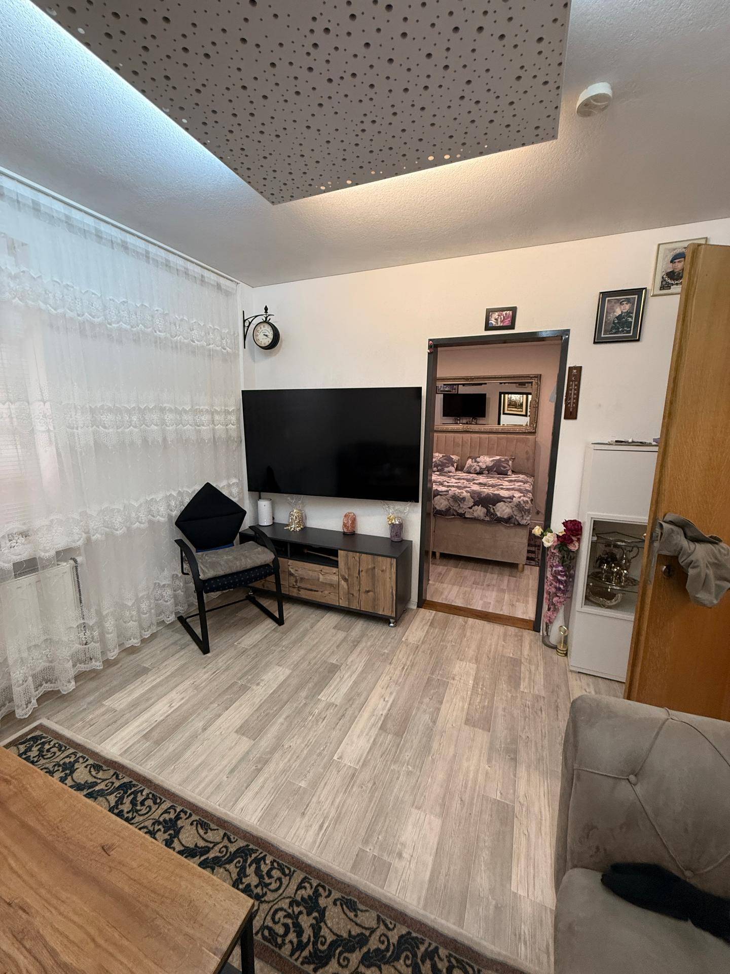 Gemütliches Wohnzimmer mit großem Fernseher, beigem Sofa und hellem Laminatboden.