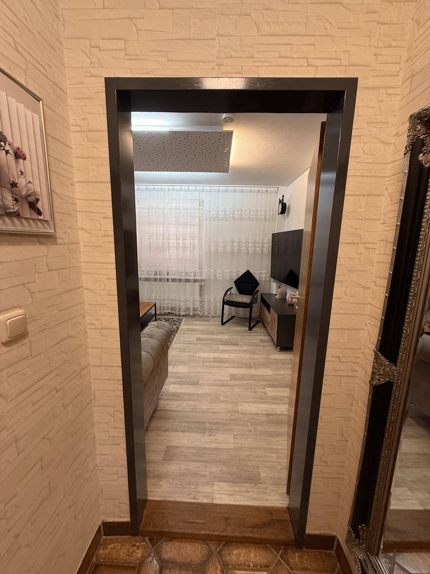 Blick durch eine Tür in ein helles Wohnzimmer mit hellem Laminatboden und modernen Möbeln.
