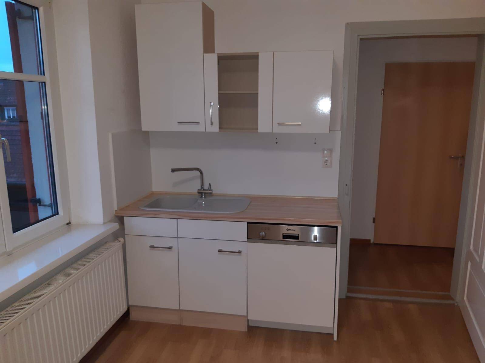 Leere Küche mit Spüle, Geschirrspüler und weißen Unterschränken unter einem Fenster.