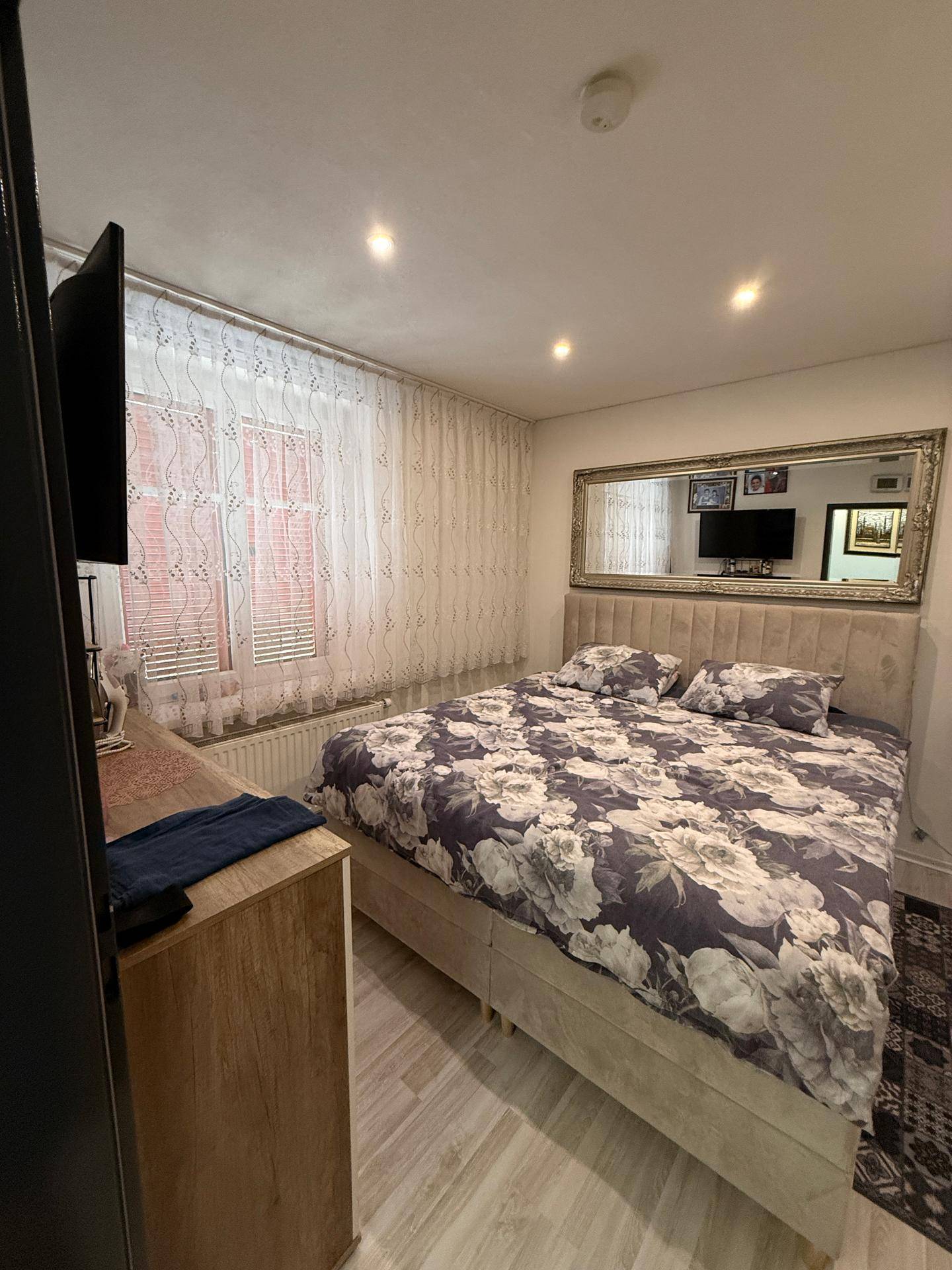 Schlafzimmer mit großem Bett, floraler Bettwäsche und einem Spiegel über dem Kopfteil.