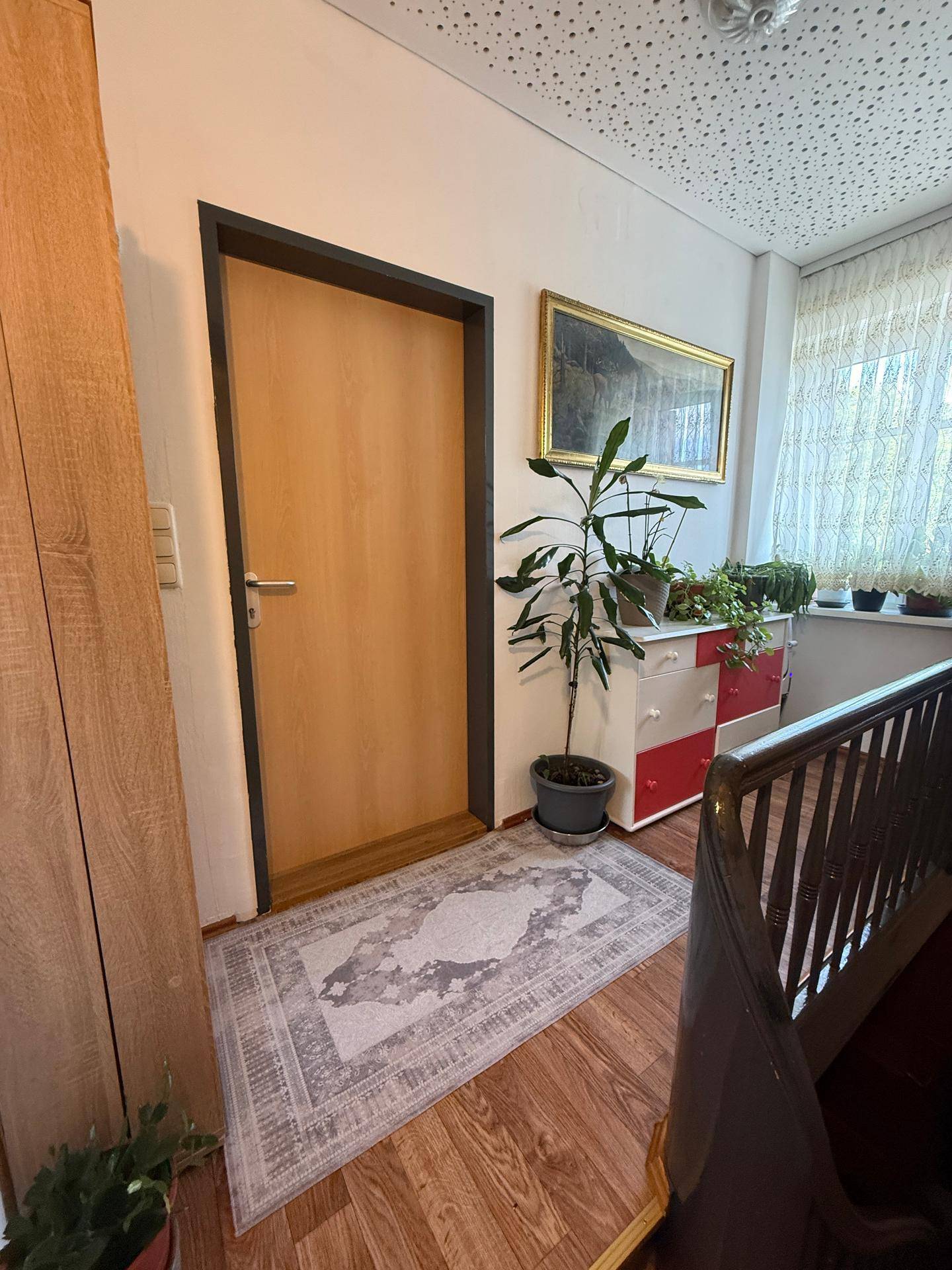 Heller Flur mit Holzboden, einer Tür und einem Fenster mit Blick nach draußen.