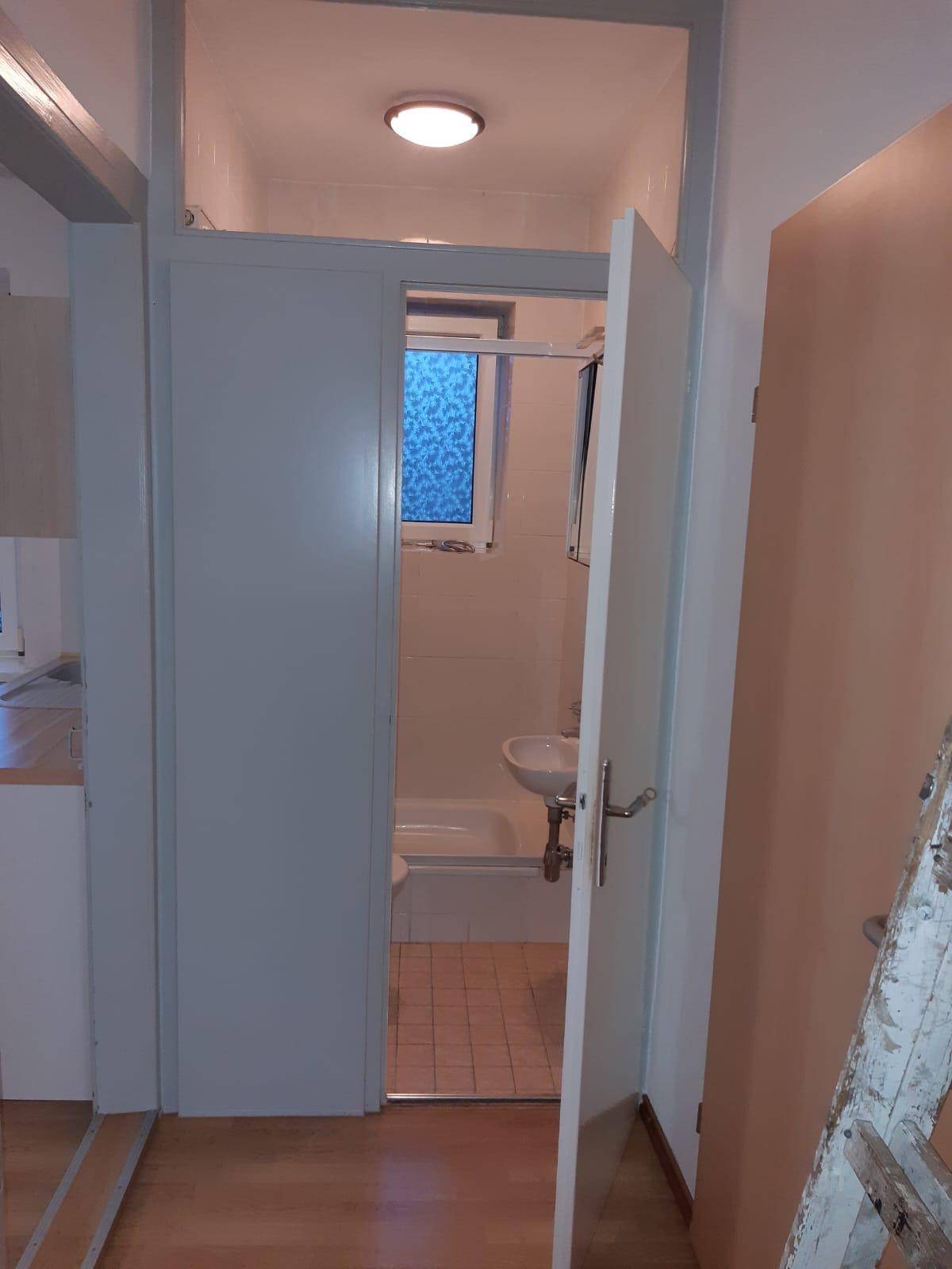 Blick durch eine offene Tür in ein Badezimmer mit Badewanne, Waschbecken und Fenster.