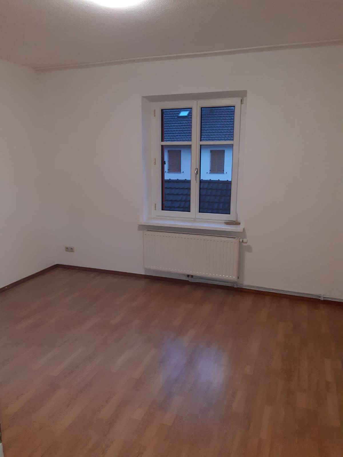 Leeres Zimmer mit hellem Laminatboden, weißen Wänden und einem Fenster.