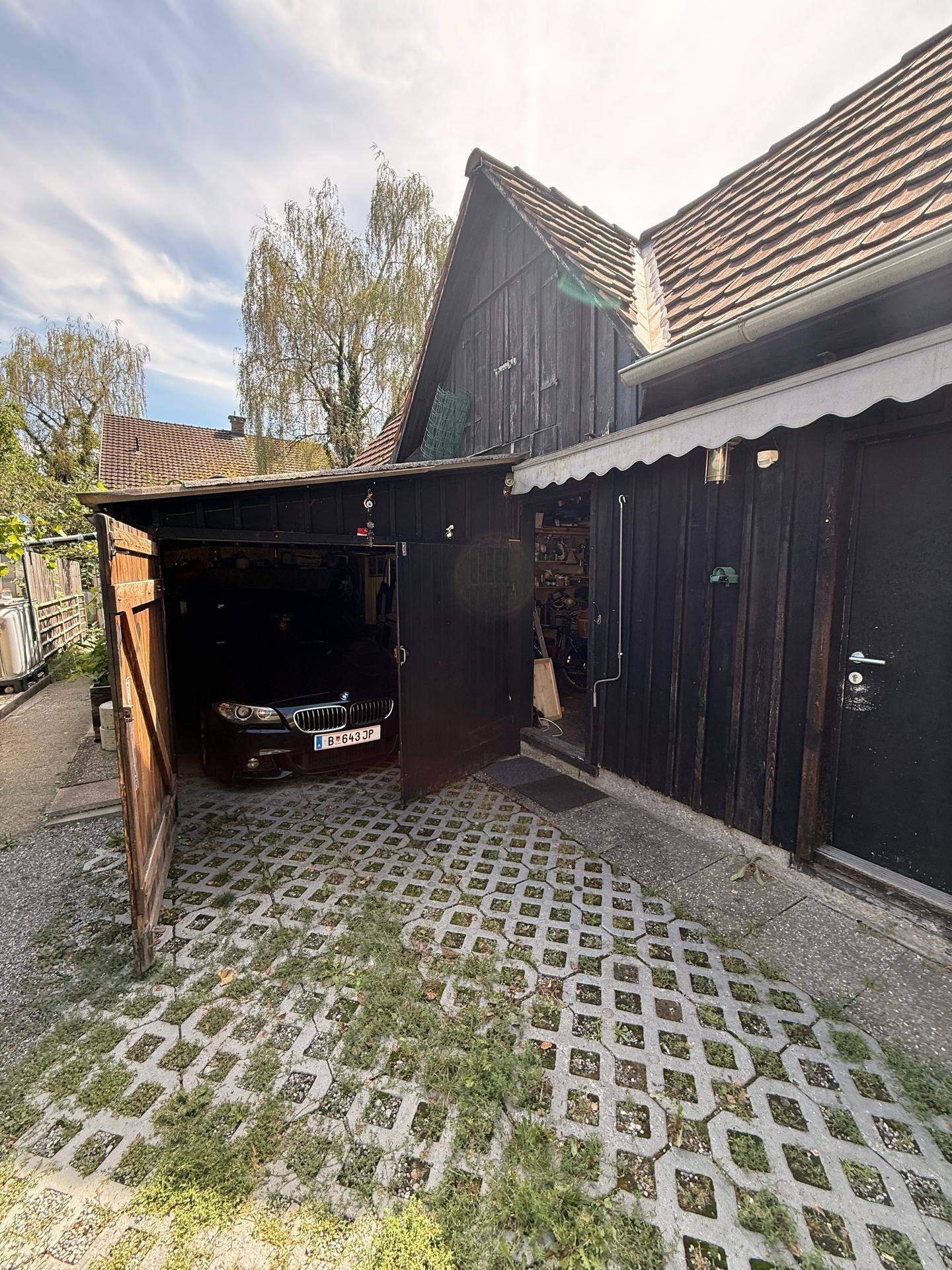 Offene Garage mit einem geparkten Auto und einem gepflasterten Bereich davor.